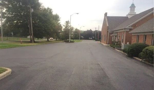 Asphalt road leading past a red brick building with a steeple. Cloudy day.