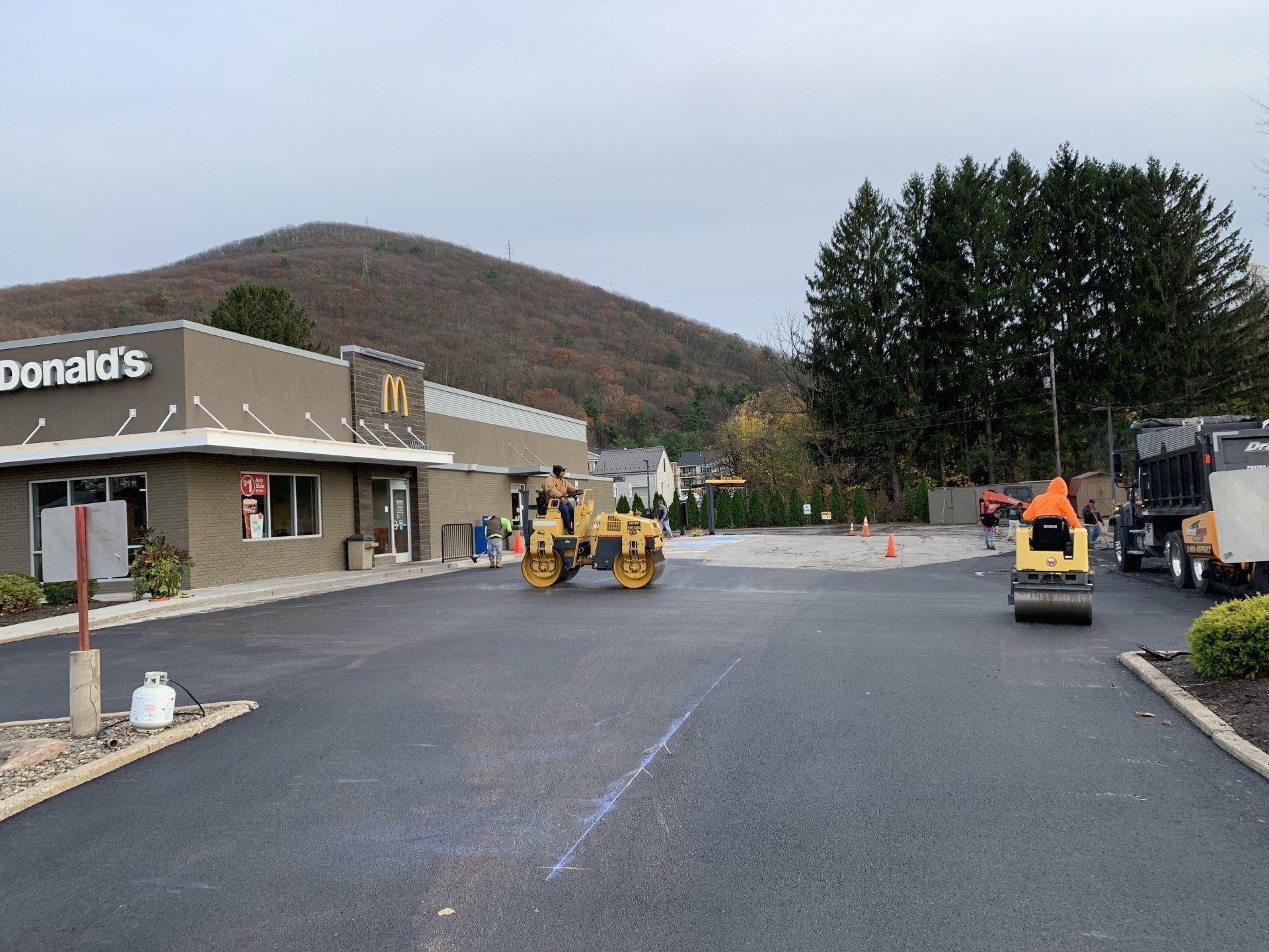 Asphalt paving at McDonald's. Yellow roller compacts asphalt. Construction crew, trucks, and mountain in the background.