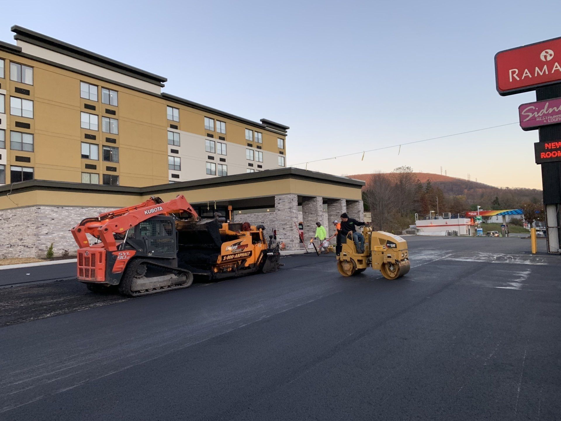 Paving construction at a hotel entrance with heavy machinery; a roller and a small Bobcat compact track loader are present.