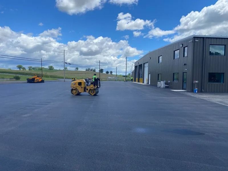 Workers using rollers to pave a parking lot in front of a commercial building.