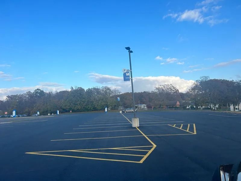 Empty asphalt parking lot on a sunny day, with yellow lines and a tall light pole.