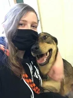 Person in a black mask posing with a happy brown dog indoors