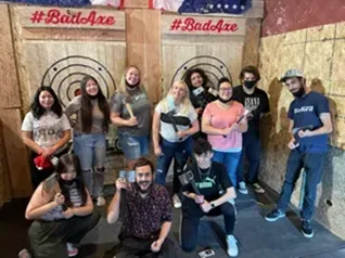Group posing with axe-throwing targets and #BadAxe signs in a recreational venue