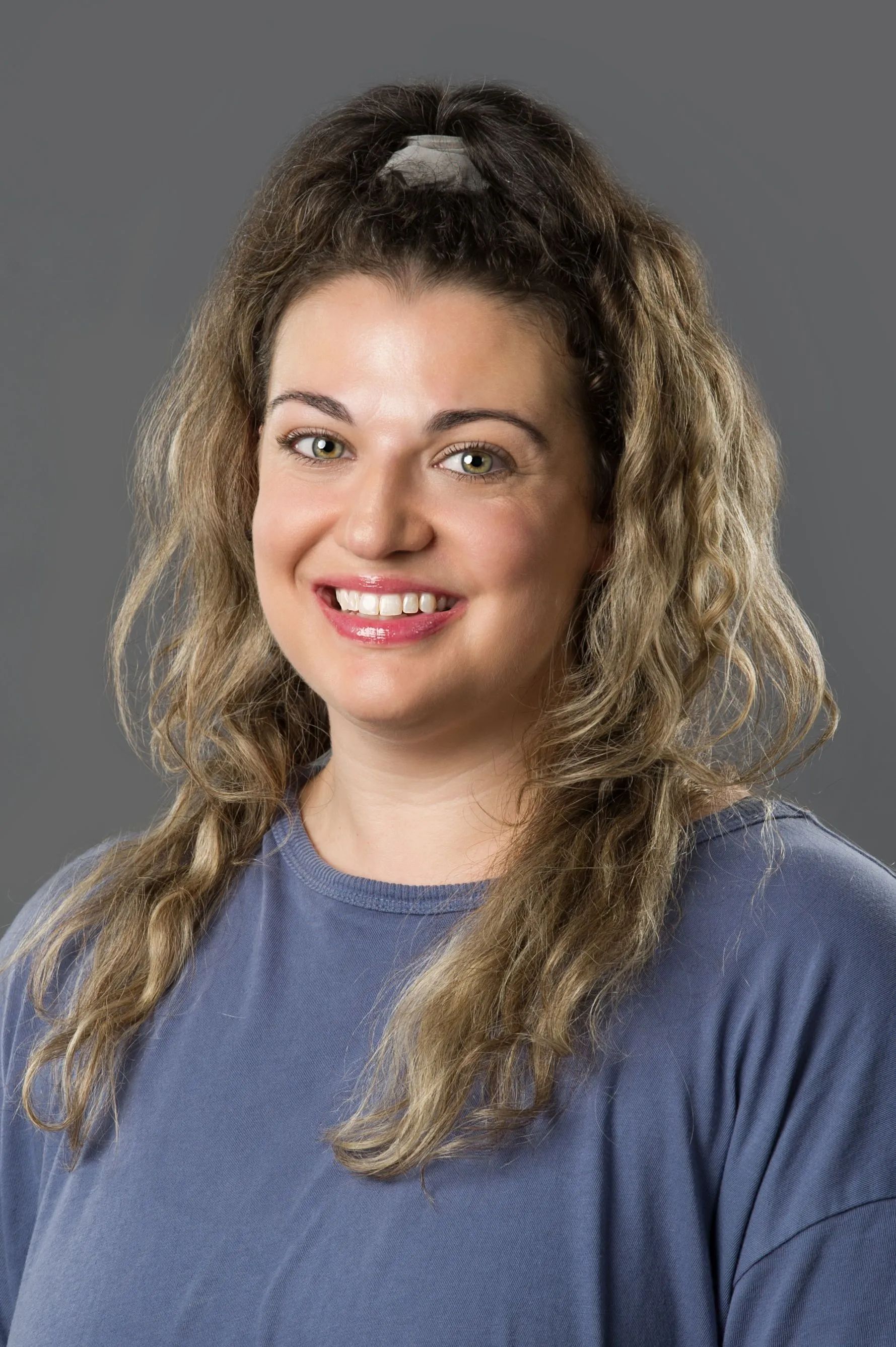 Portrait of a smiling person with curly hair in a blue sweater against a gray background