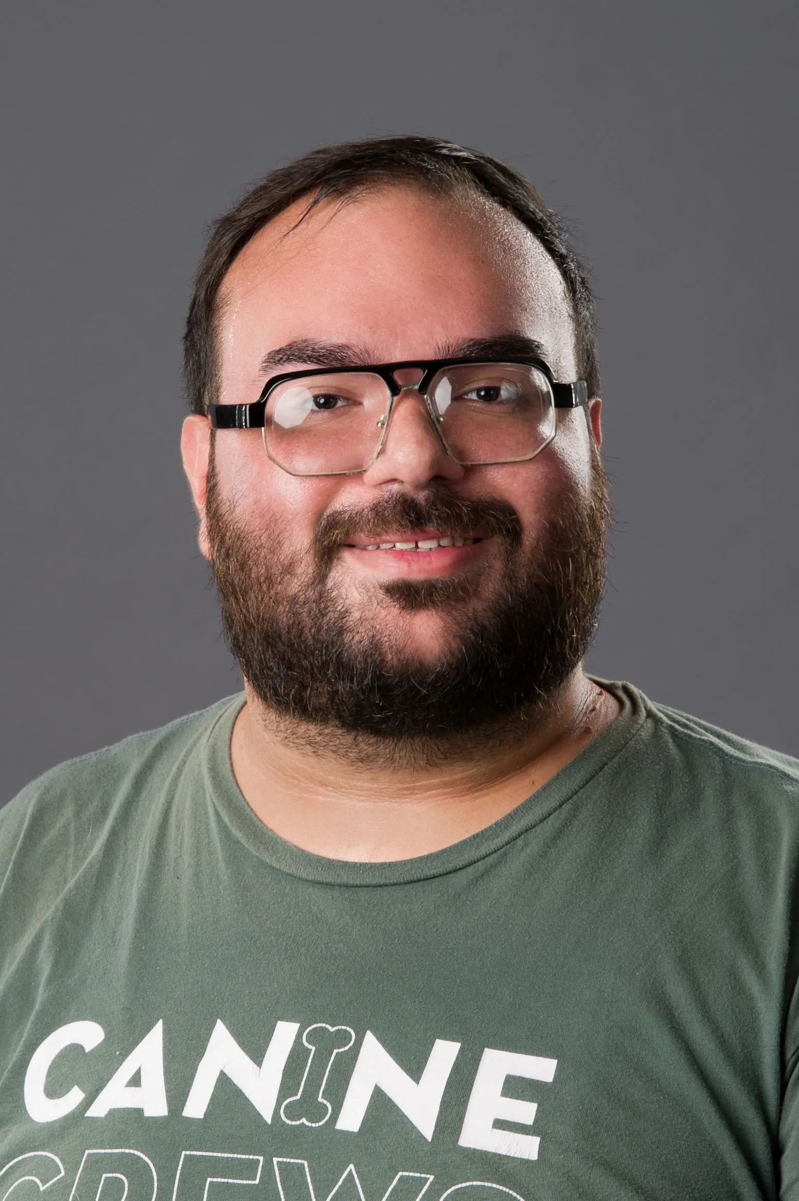 Smiling bearded man wearing glasses and a green T-shirt against a gray background