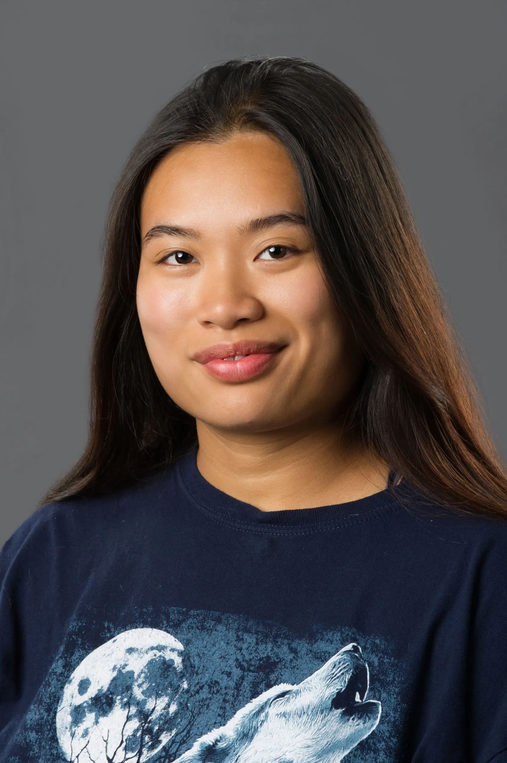 Portrait of a person with long dark hair wearing a navy wolf graphic T-shirt against a gray background