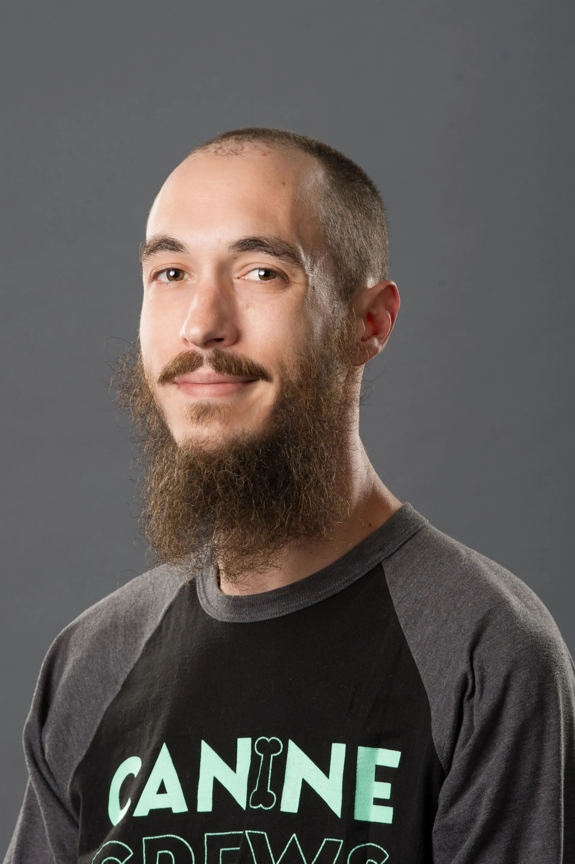 Portrait of a man with a long beard wearing a black and gray shirt against a plain gray background