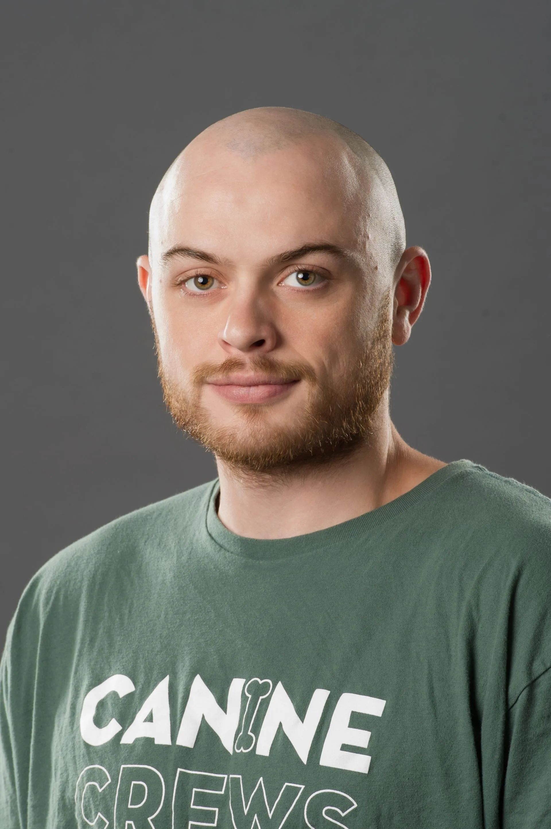 Portrait of a bald man with a short beard wearing a green T-shirt against a gray background