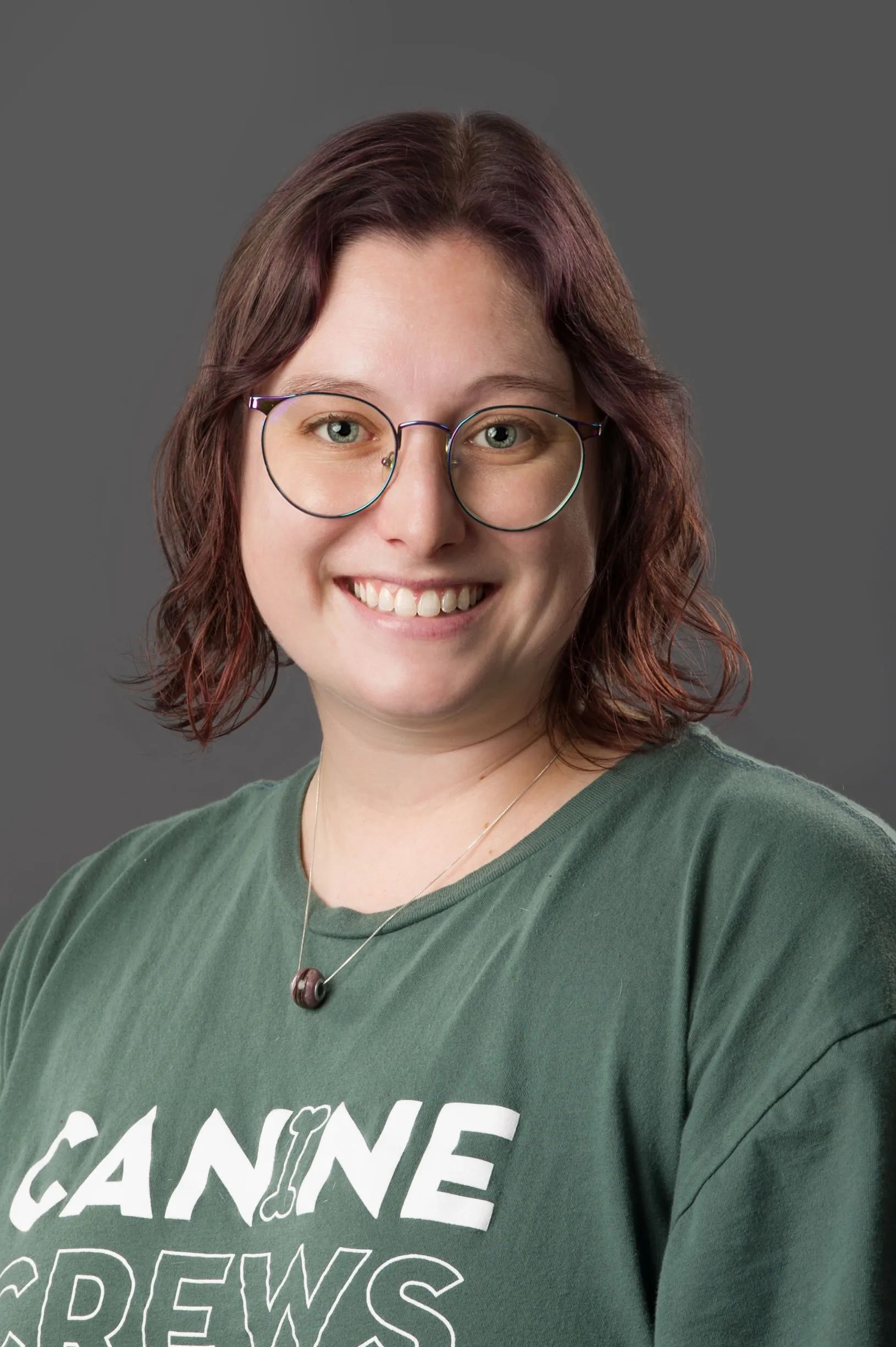 Smiling person with glasses in a green shirt against a gray background