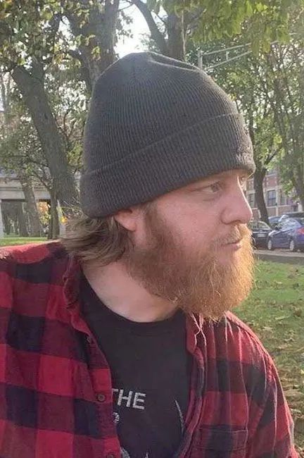 Person in a gray beanie and red plaid shirt looking right in a sunlit park