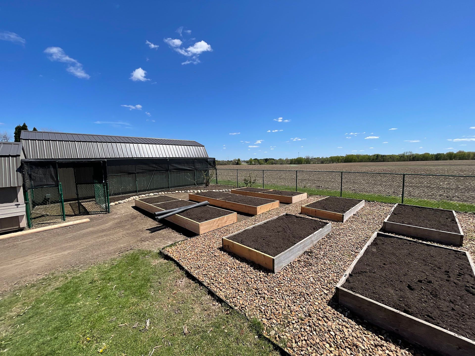 a row of raised garden beds in a yard with a greenhouse in the background