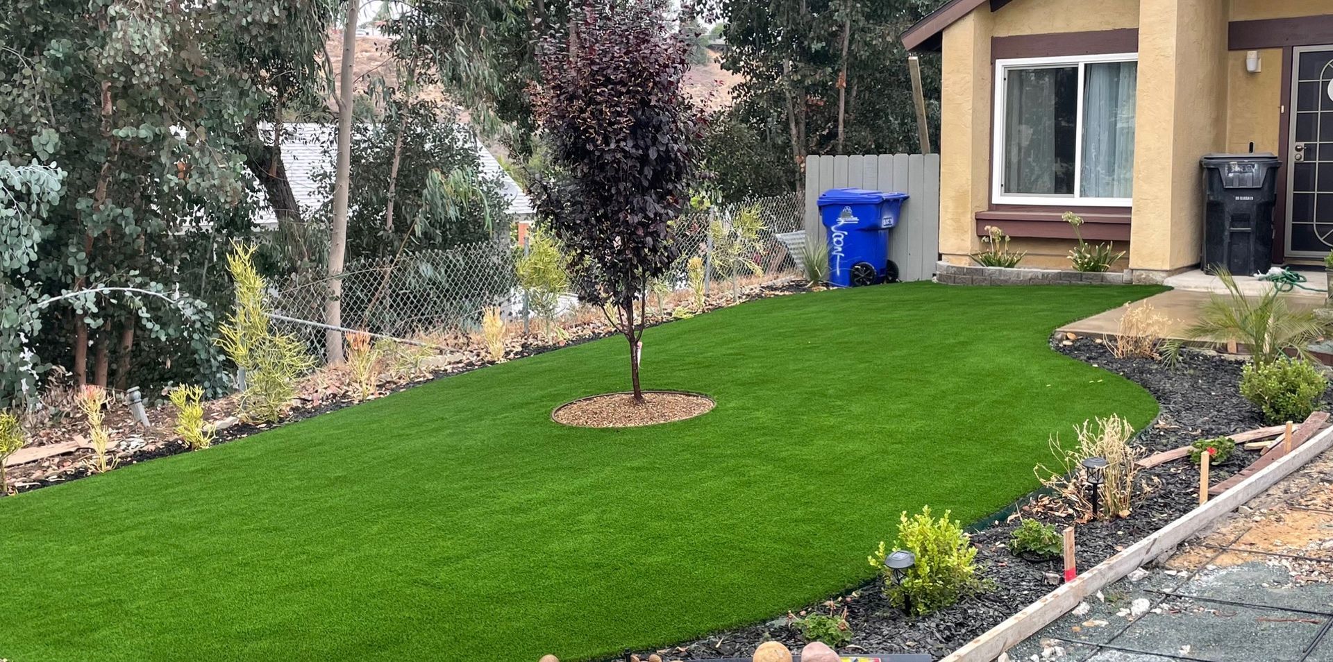 Gravel driveway bordered by plants and rocks; garden bed with red flowers - after.