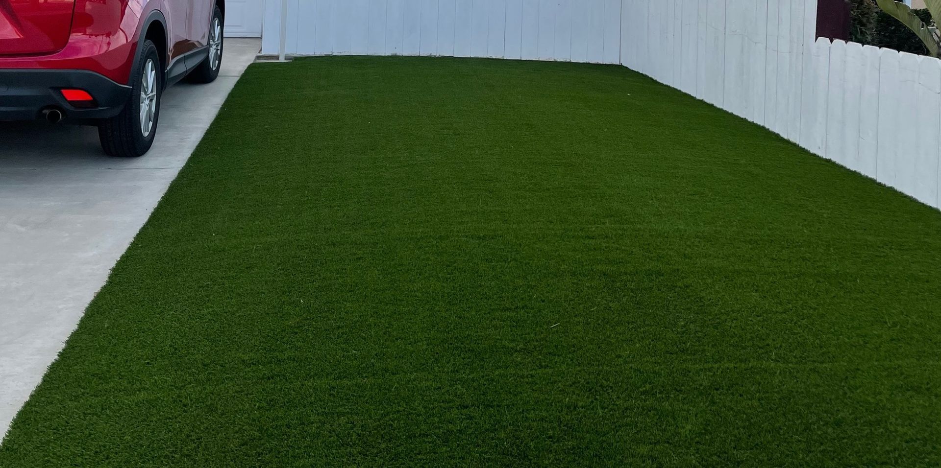 Person in green shorts standing near a car and a dirt patch in front of a white fence - after.