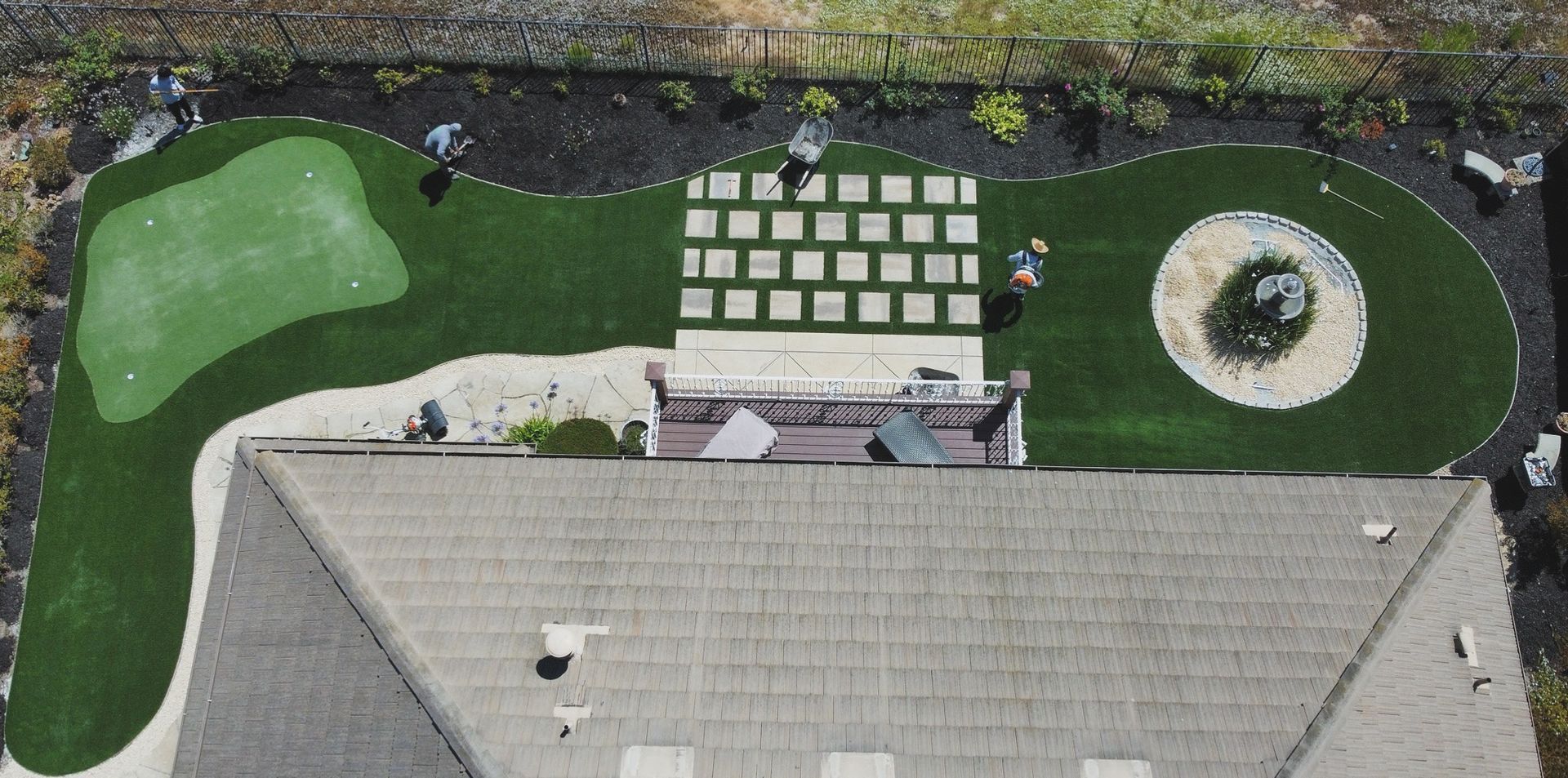 Aerial view of a house with a gray roof and a backyard lawn with landscaping and a small water feature - after.