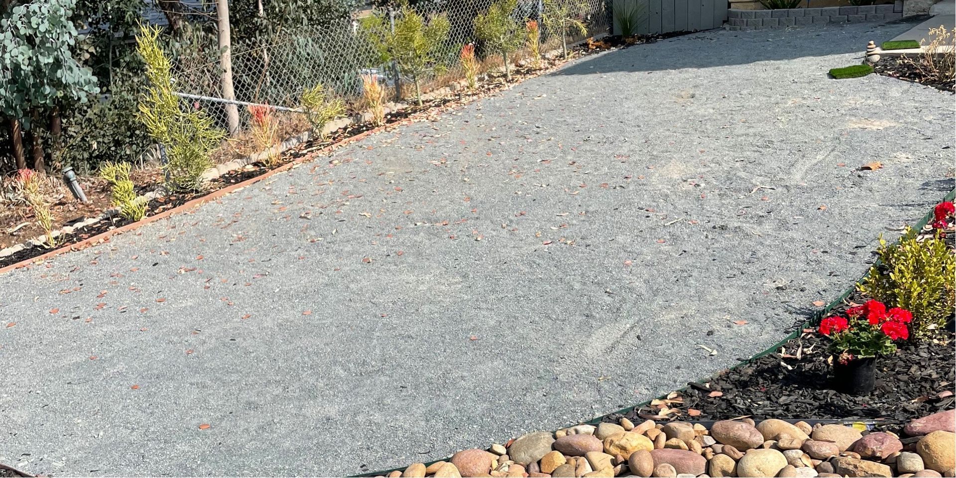 Gravel driveway bordered by plants and rocks; garden bed with red flowers - before.