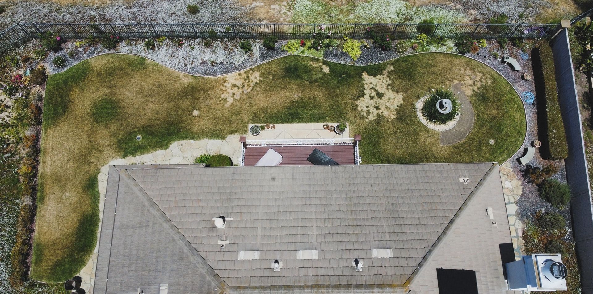 Aerial view of a house with a gray roof and a backyard lawn with landscaping and a small water feature - before.