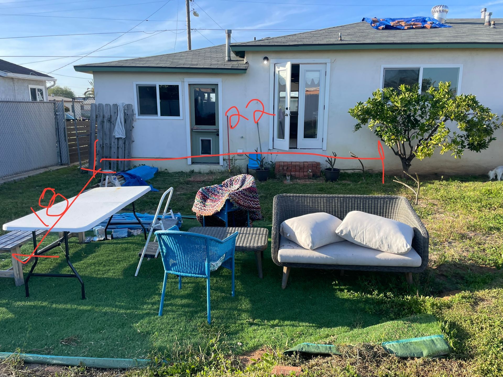 Backyard scene: white house with open doors, patio furniture on green turf, and a small tree.