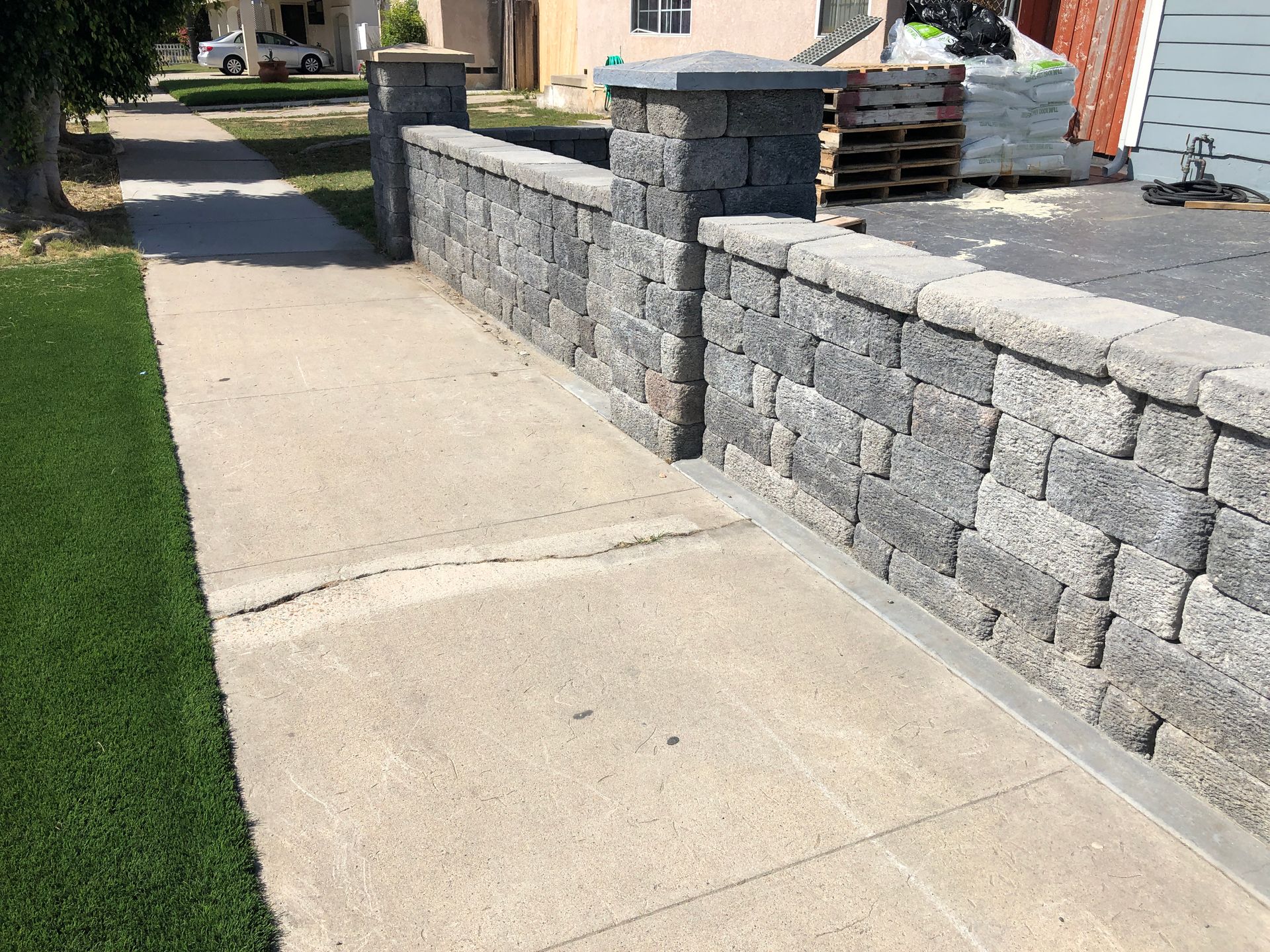 Concrete sidewalk with a gray block wall alongside a grassy lawn.