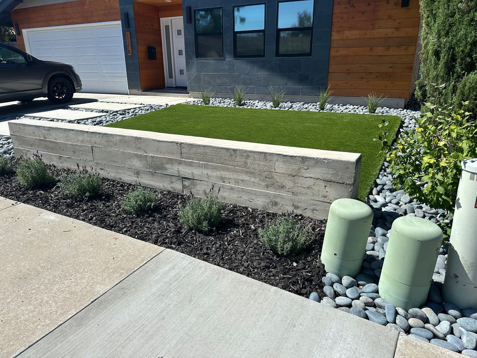 Modern home exterior with concrete wall, artificial turf, black gravel, and decorative pillars.