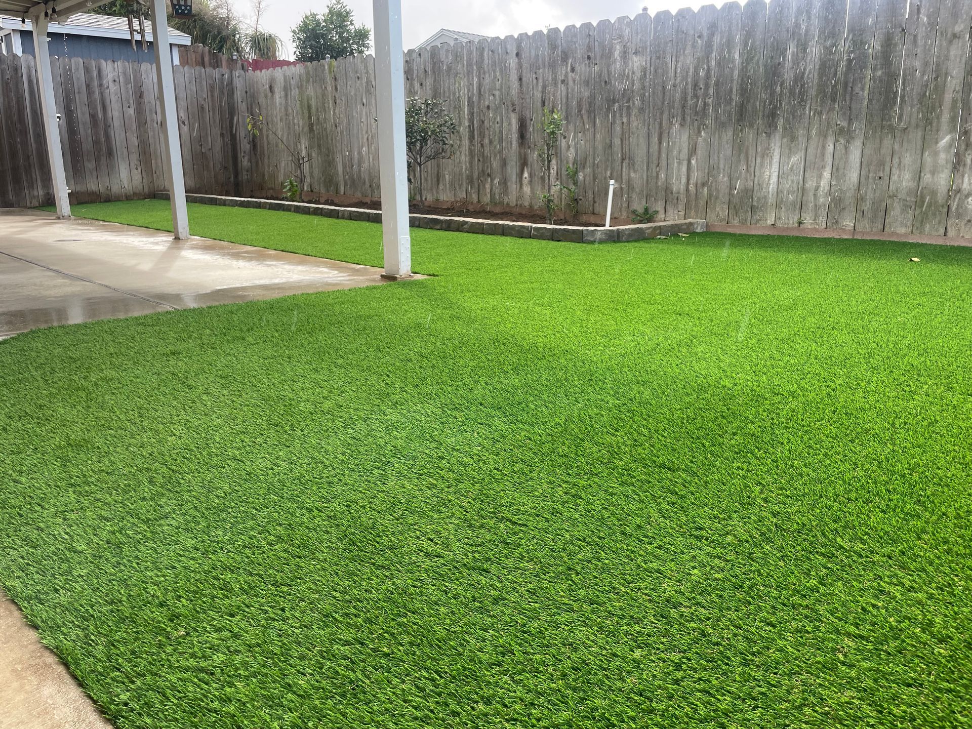 Green artificial turf in a backyard with a wooden fence and a covered patio.