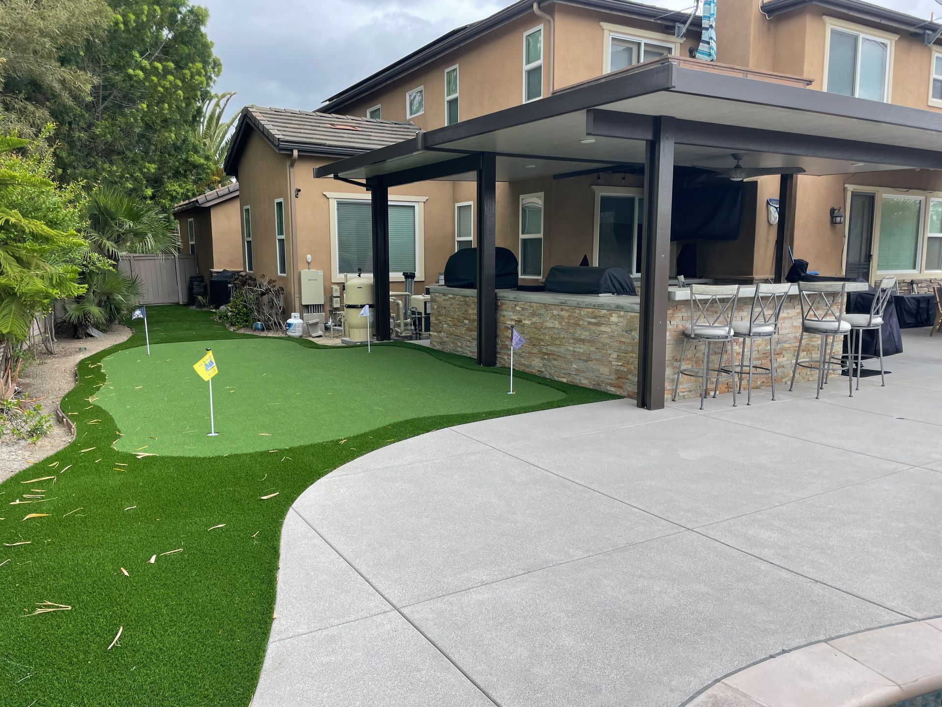 Backyard with putting green, patio, outdoor bar, and two-story house.