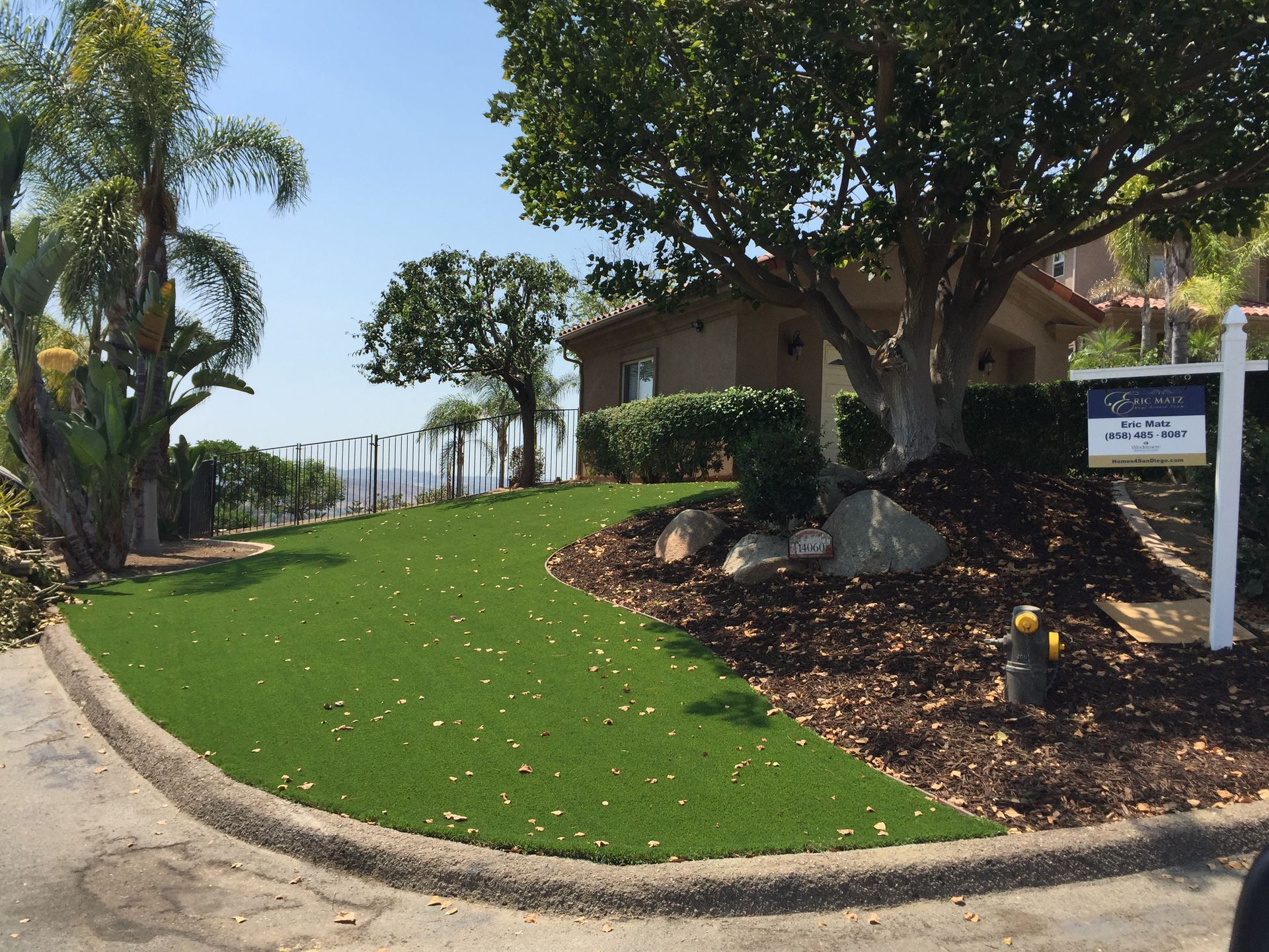 Green artificial lawn with a building and sign, trees, and blue sky.