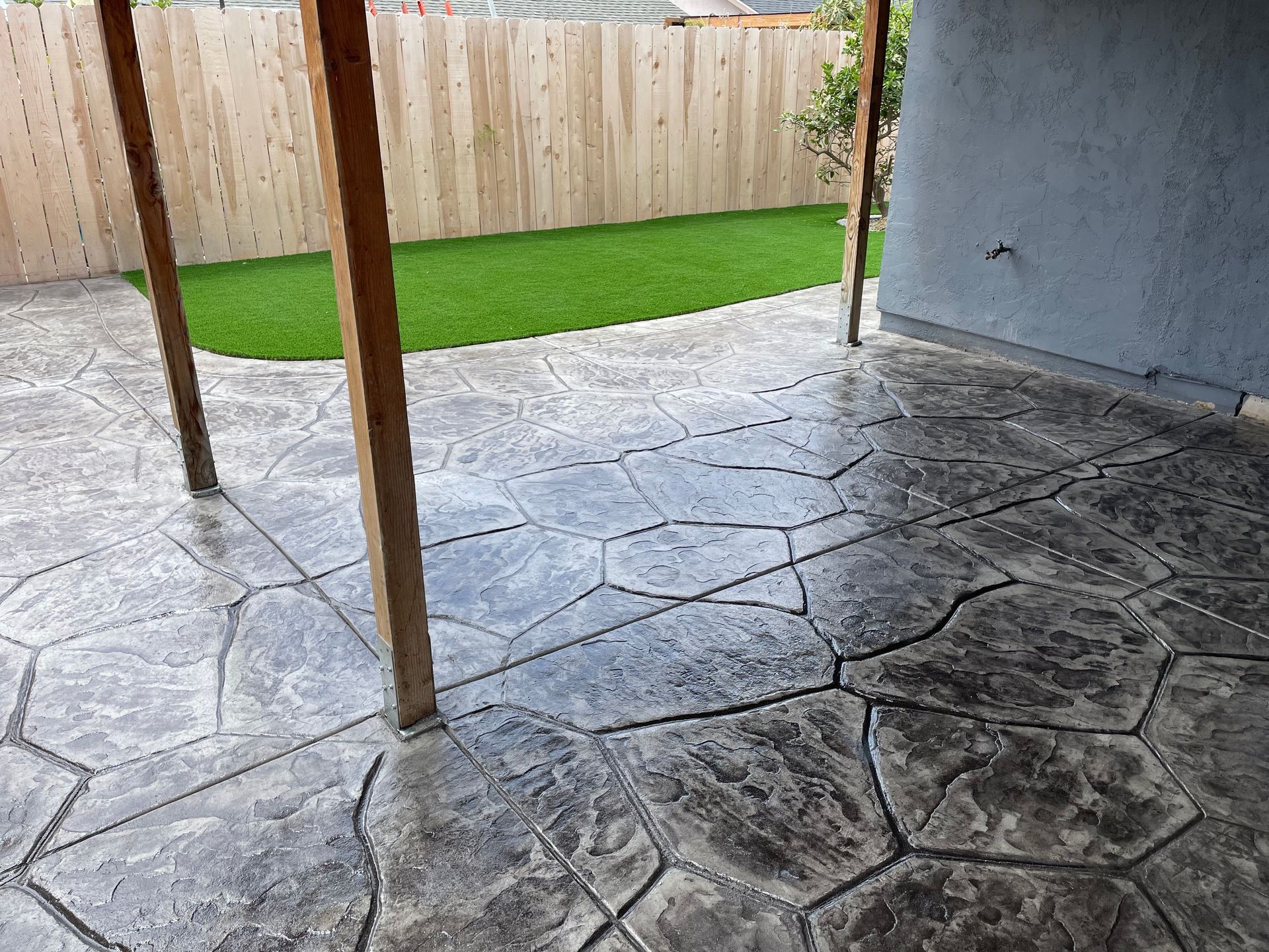 Stamped concrete patio with a wooden fence and artificial turf in the background.