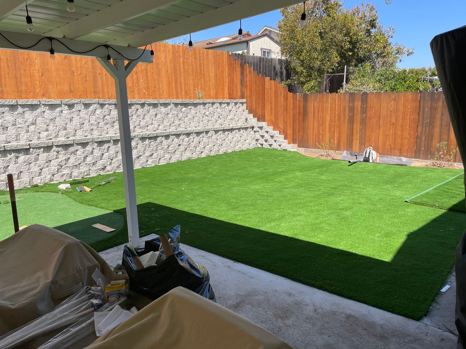 Backyard with artificial turf, wooden fence, retaining wall, and patio cover.