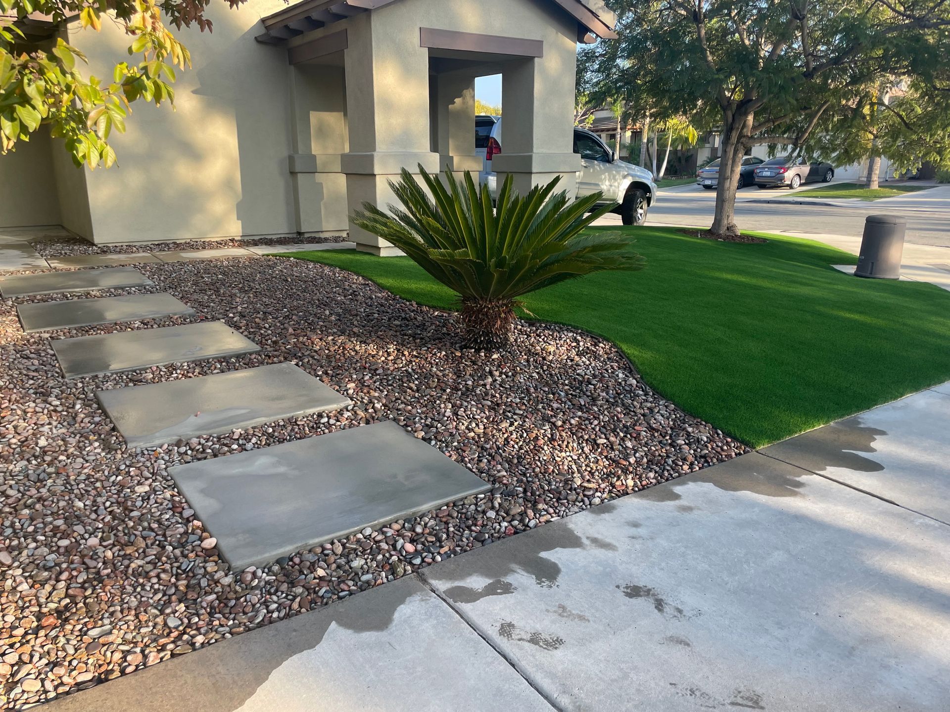 Front yard with a rock bed, stepping stones, small palm tree, and green grass.