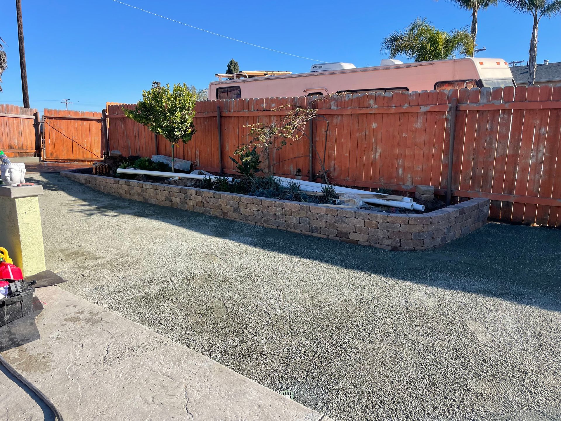 Backyard with gravel ground, brick-lined garden bed, orange wooden fence, and clear blue sky.