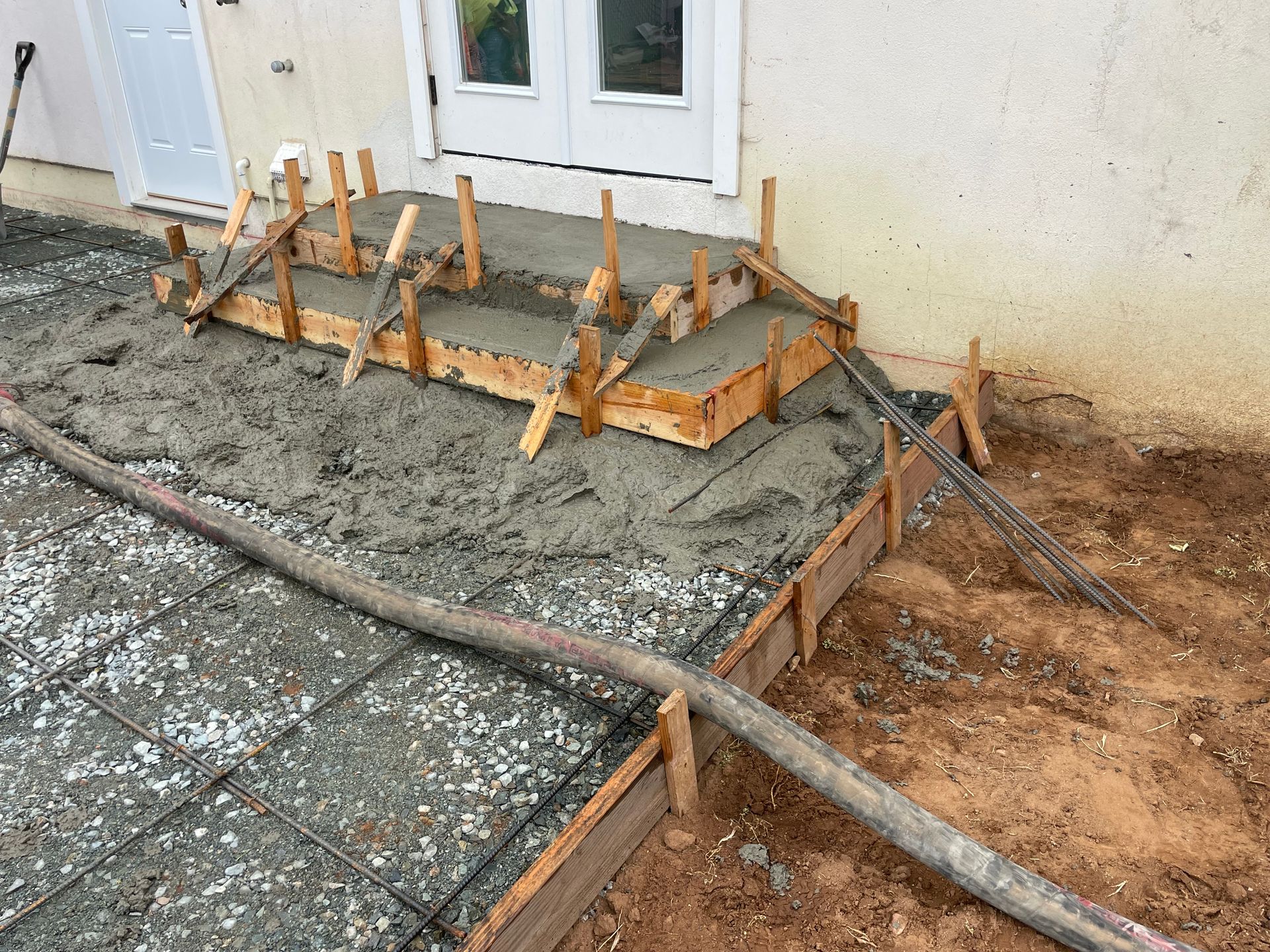 Concrete steps under construction outside a building. Wooden forms and a concrete pump hose are visible.