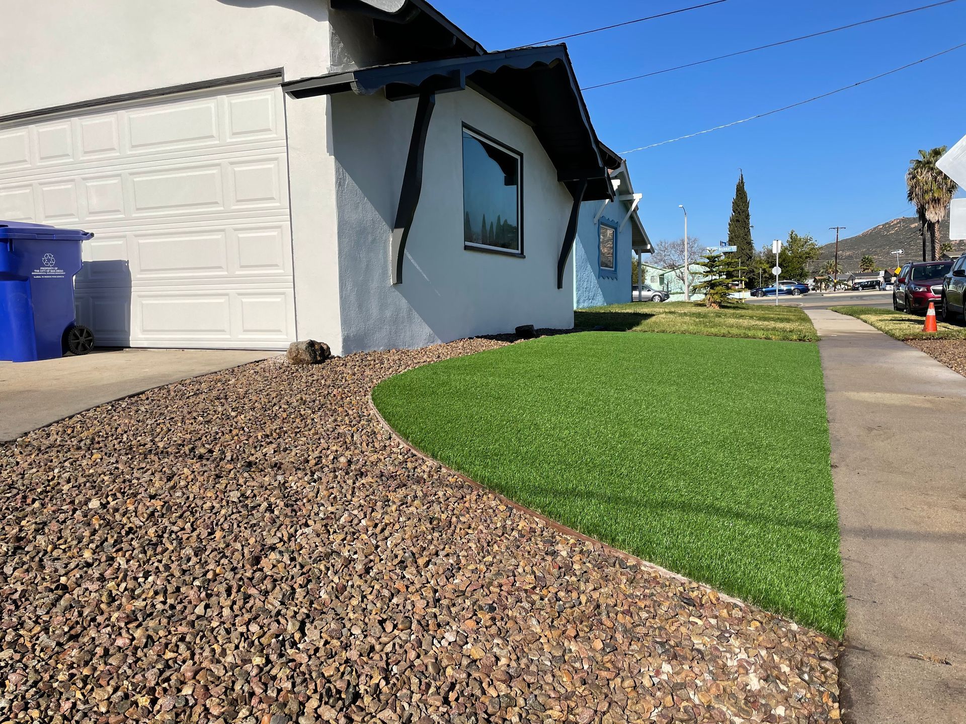 Exterior of a house with gravel and green artificial turf landscaping. Blue sky.