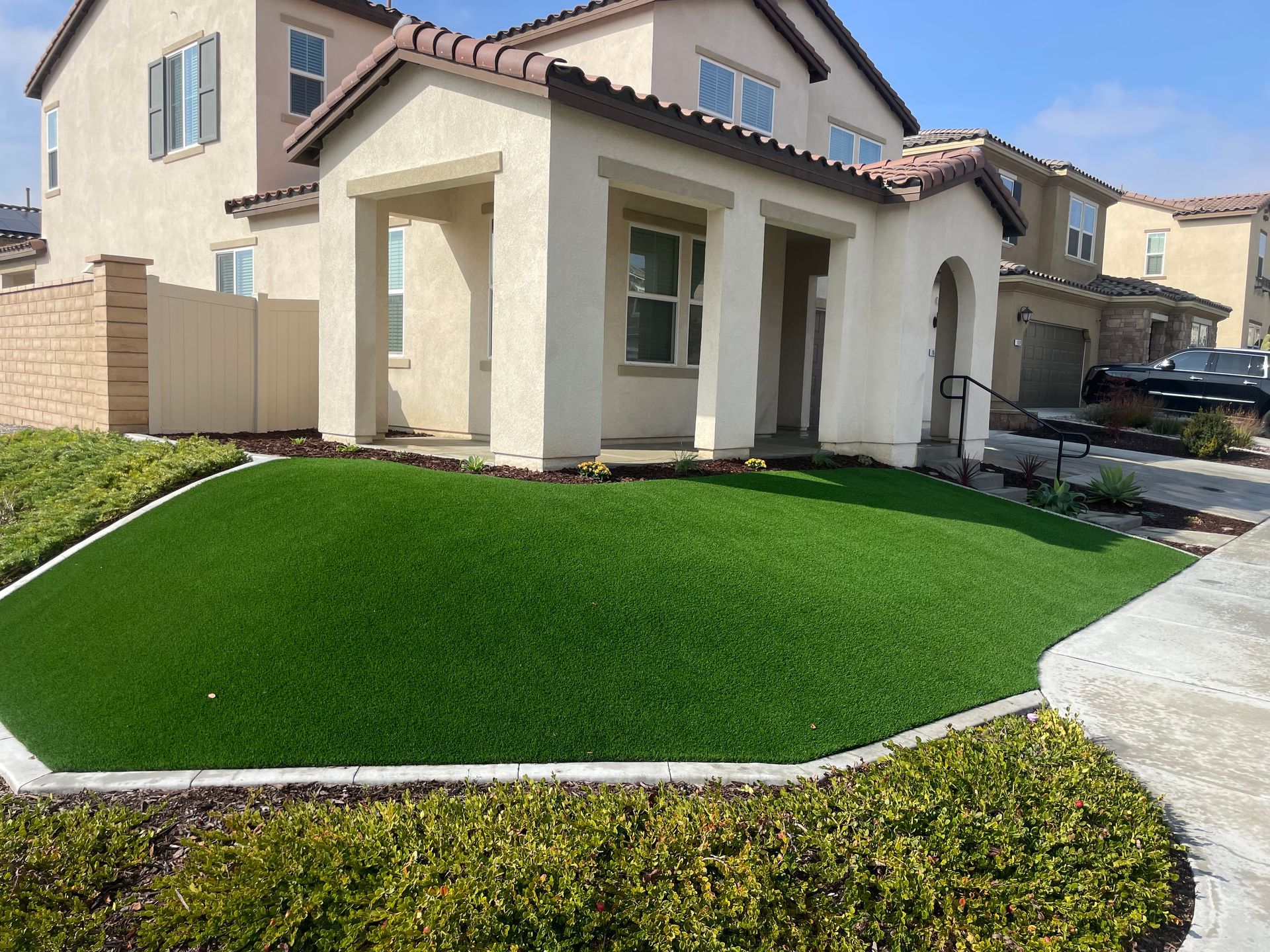 House with a manicured green artificial lawn, concrete walkway, and beige exterior.