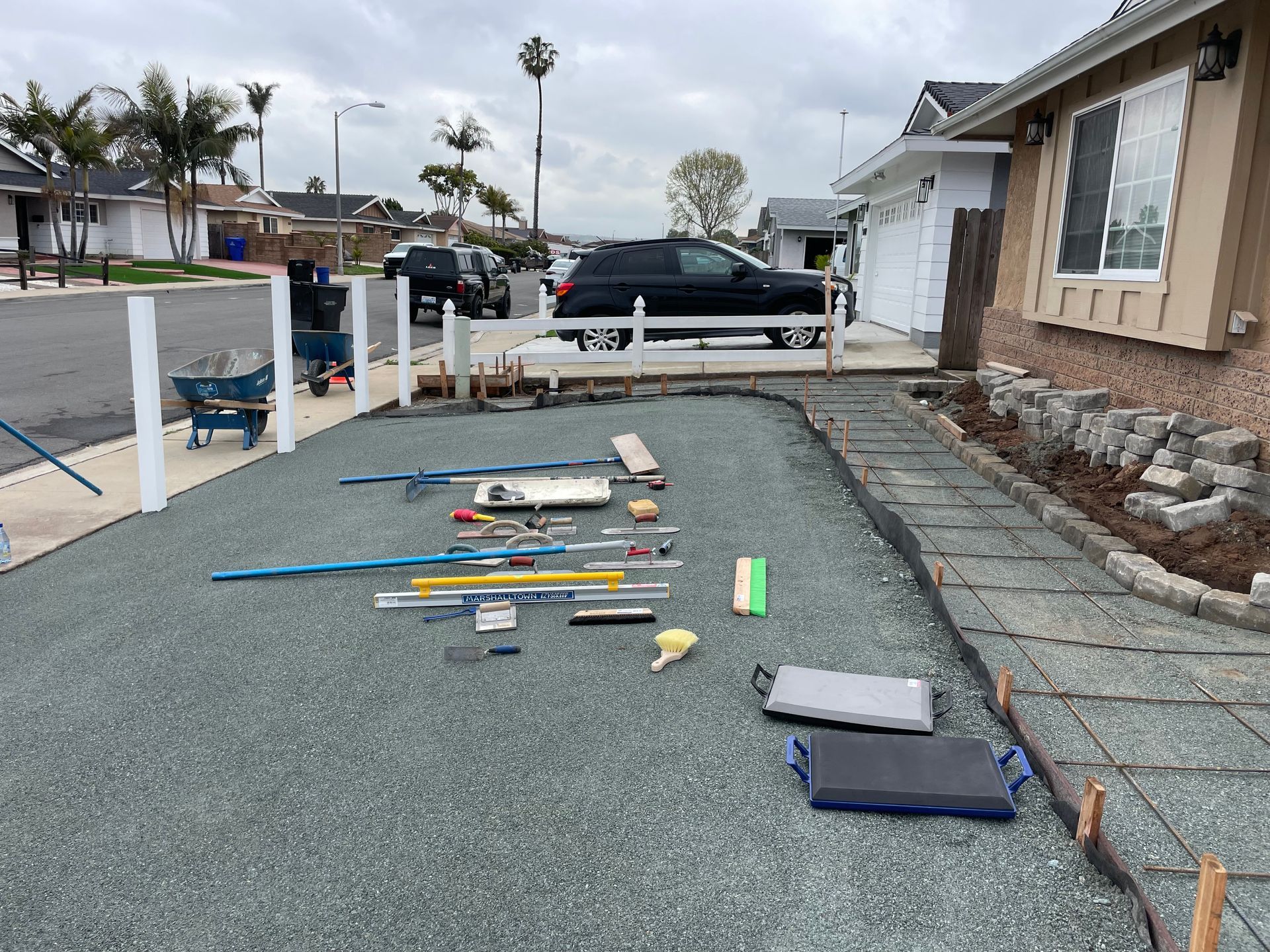Construction site: gravel and tools in front yard, pathway being built, white fence posts.
