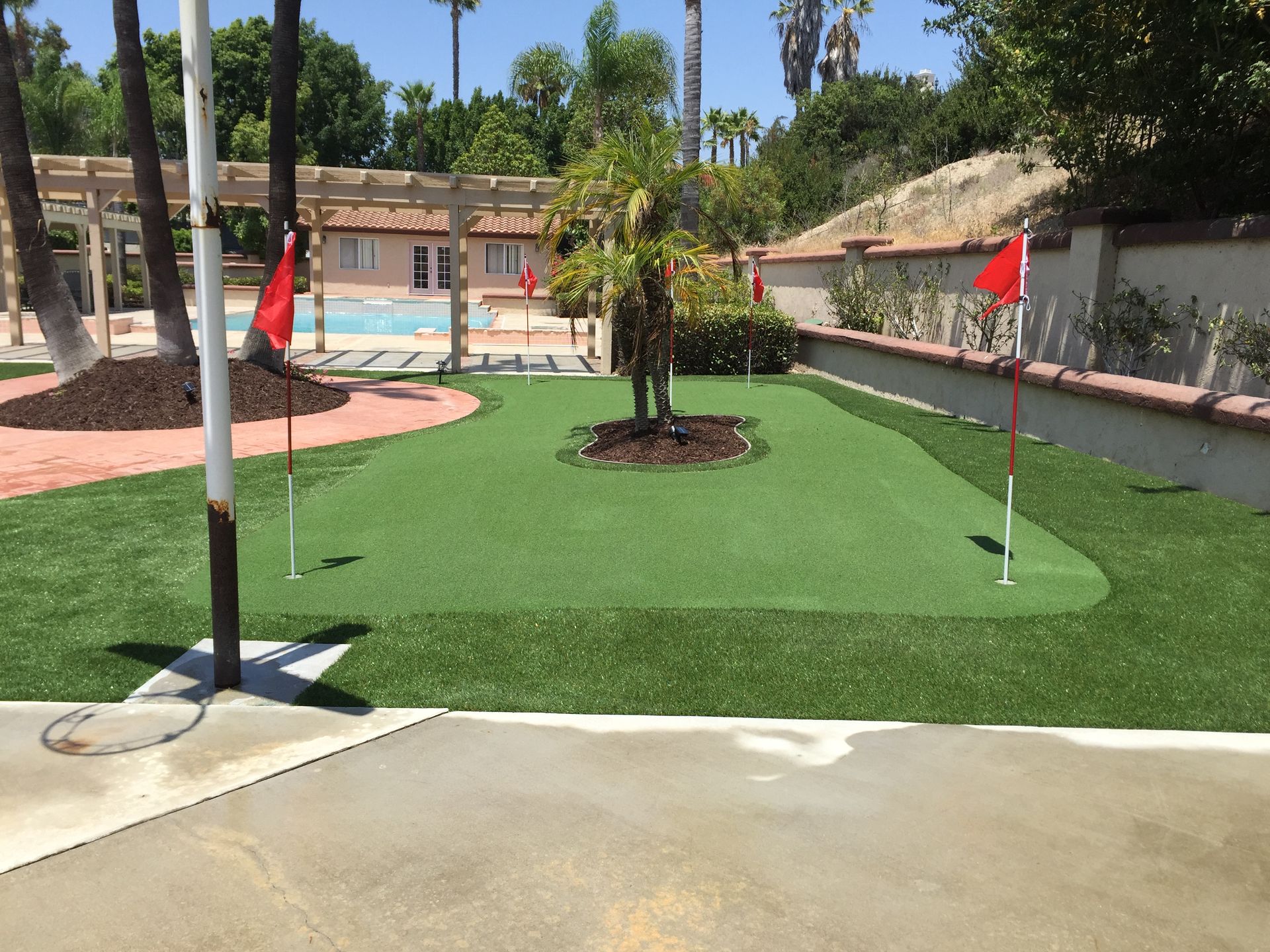 Mini golf course with green turf, red flags, and a swimming pool in the background.