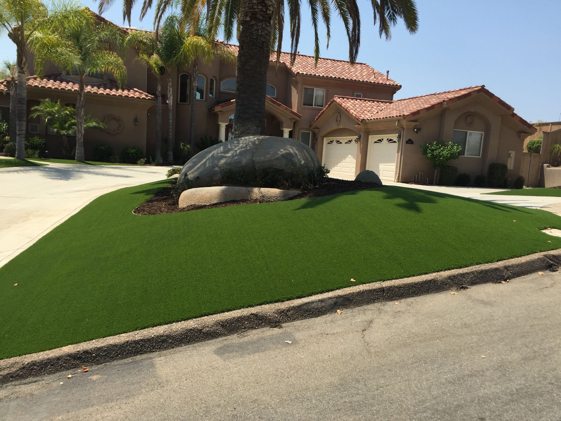 House with green lawn, large rock, and palm tree in front.