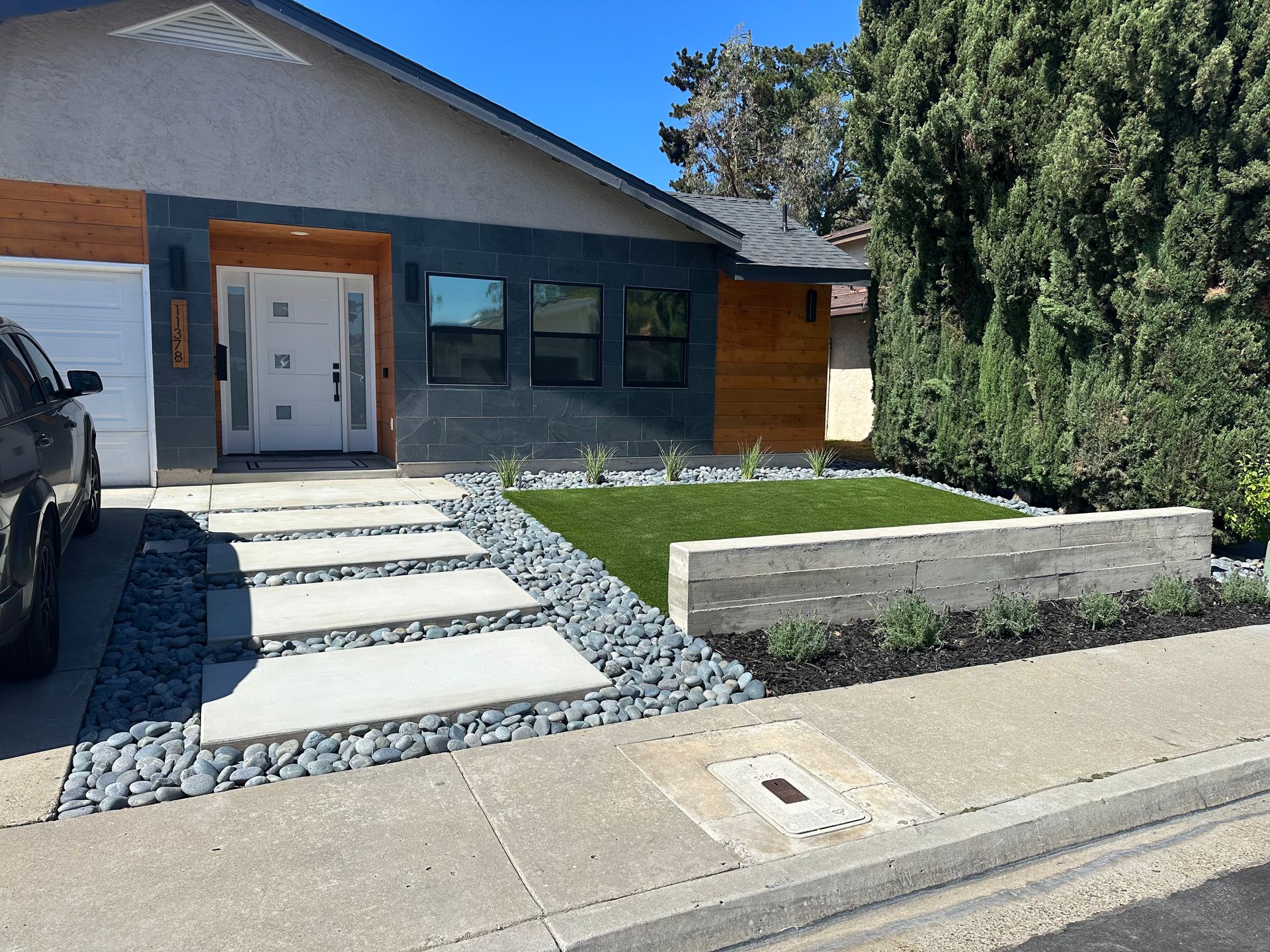 Modern home exterior with gray siding, wood accents, concrete walkway, and landscaped yard.
