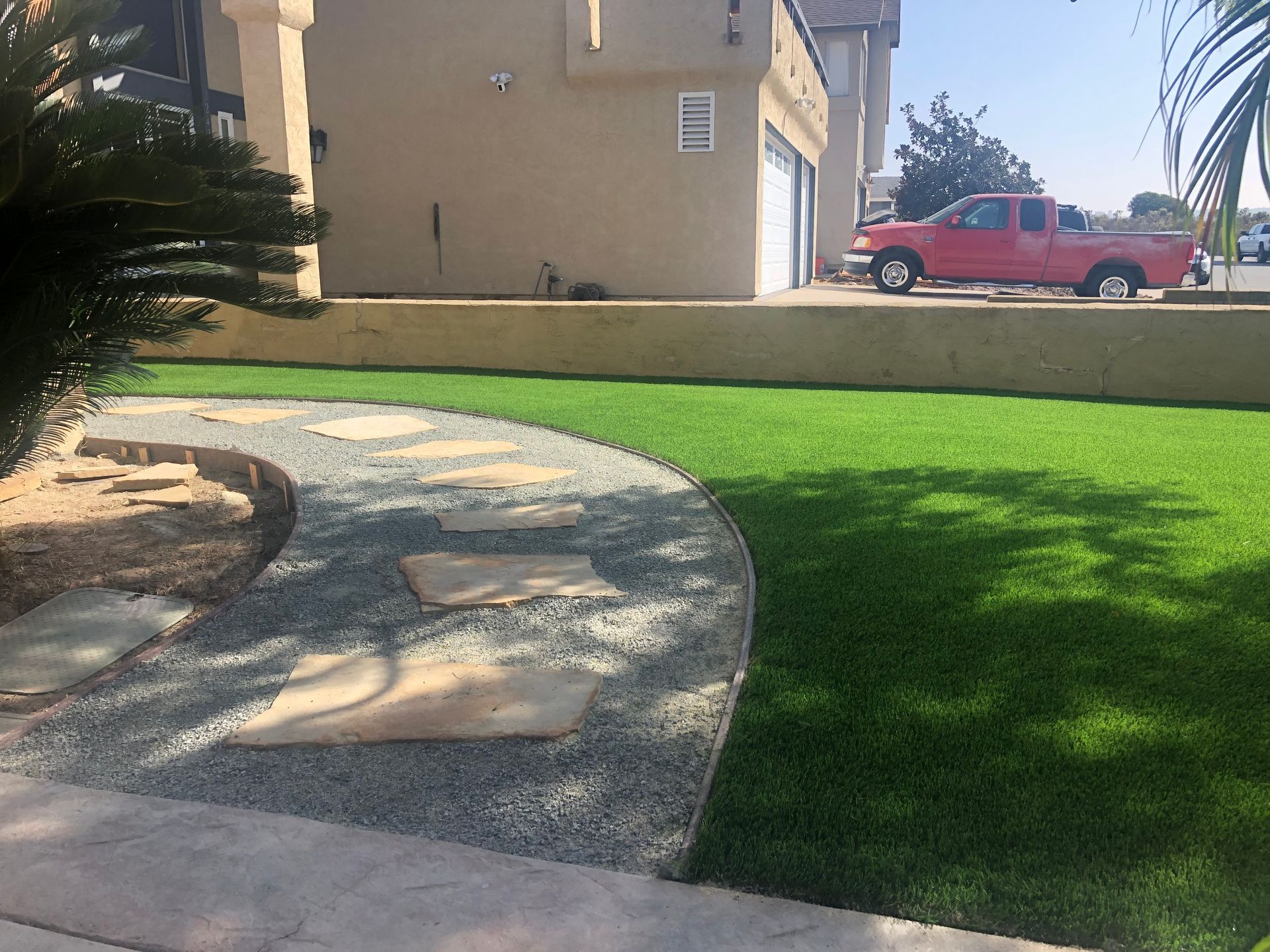 Green lawn next to a gravel path with stepping stones; a red truck is parked in the driveway.