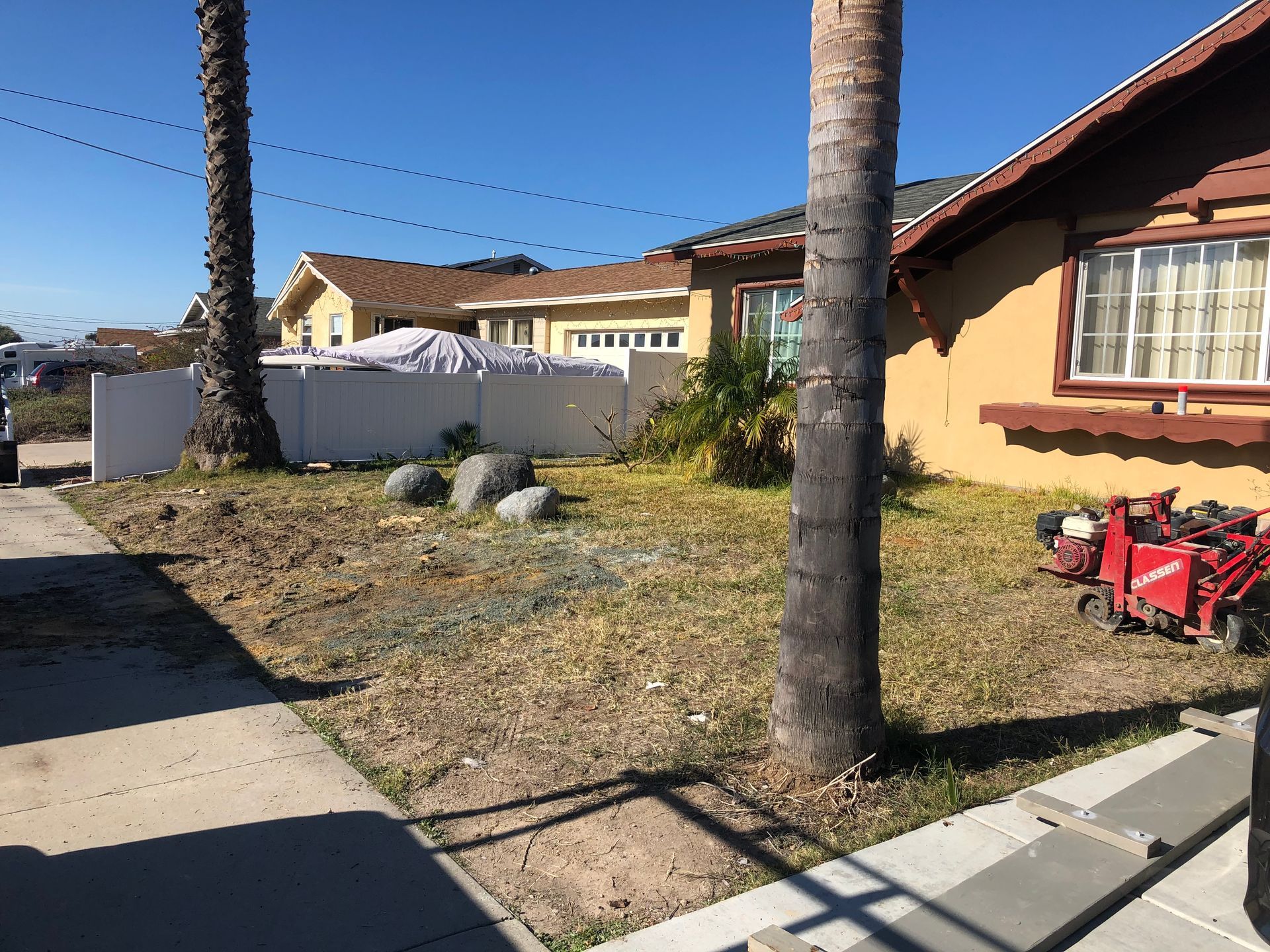 Yard with dead grass, palm trees, and a house under a clear blue sky.