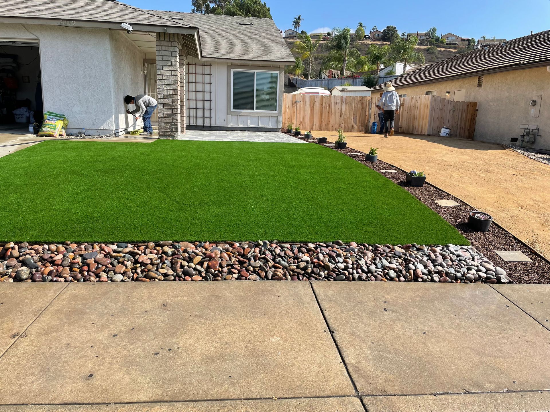 Front yard with artificial turf, rock border, gravel pathway, and a house under construction.