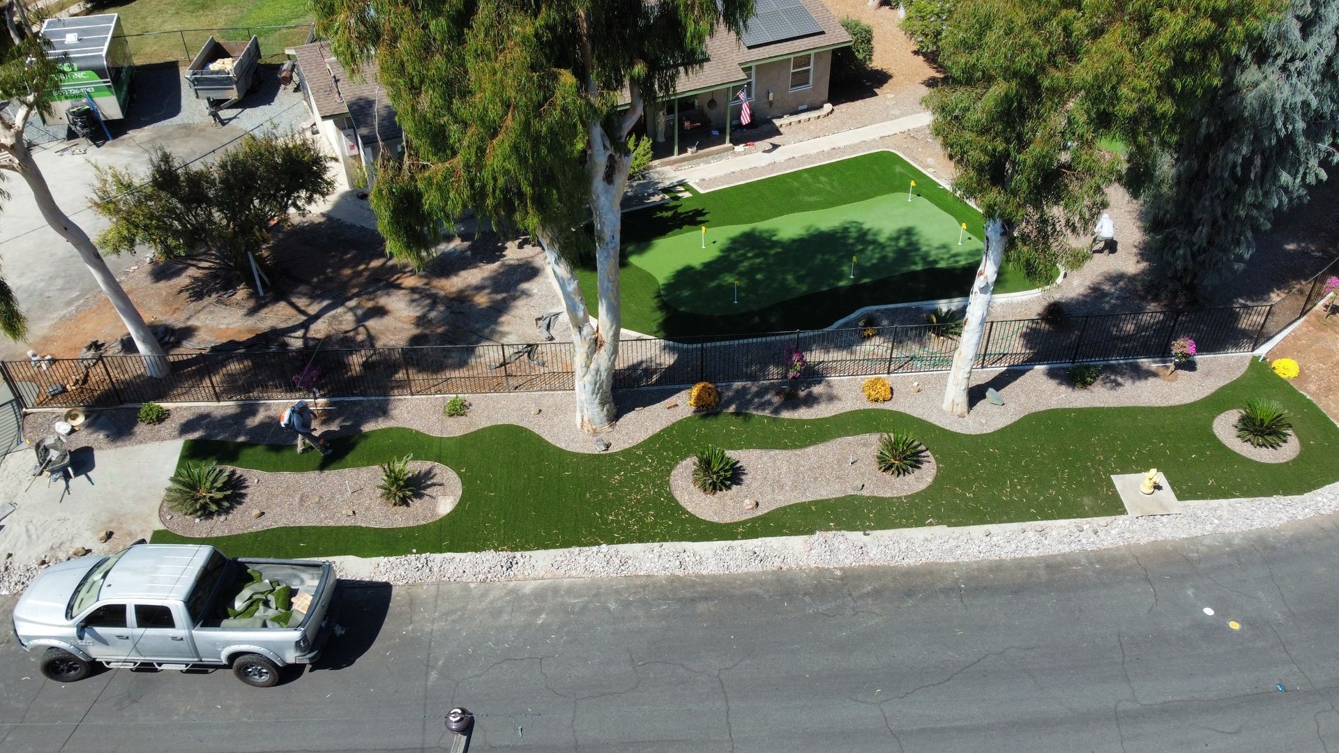 Aerial view of a home's front yard with artificial turf, a putting green, landscaping, and a truck parked at the curb.