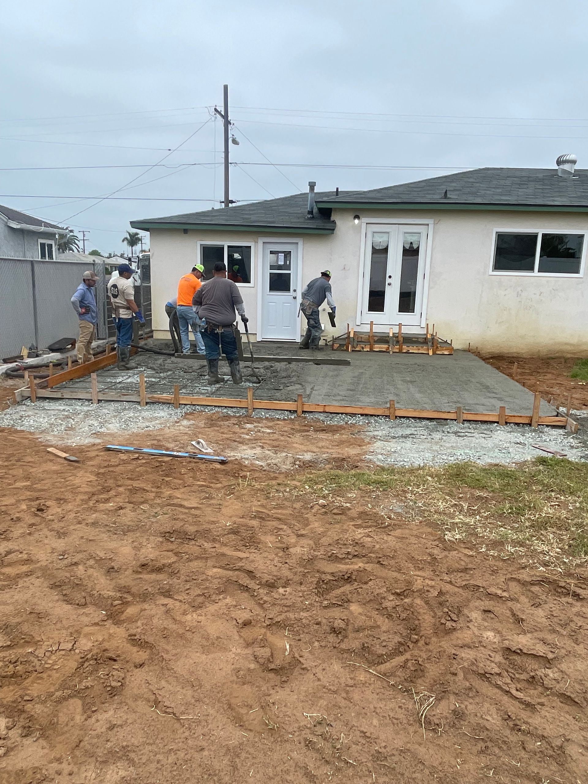 Construction workers pouring concrete for a patio behind a house on a cloudy day.