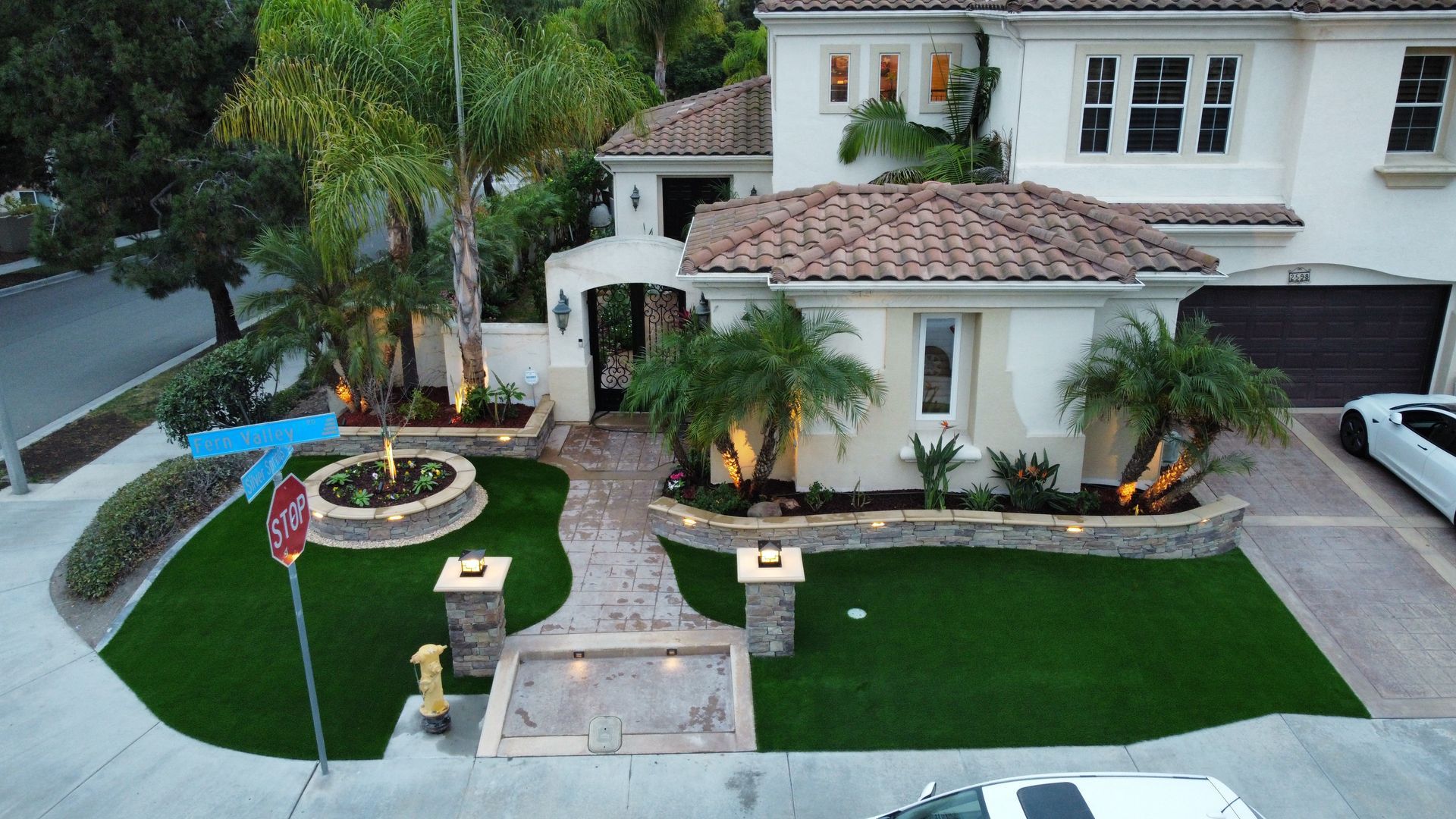 Upscale home exterior with manicured lawn, palm trees, and stone walkway.