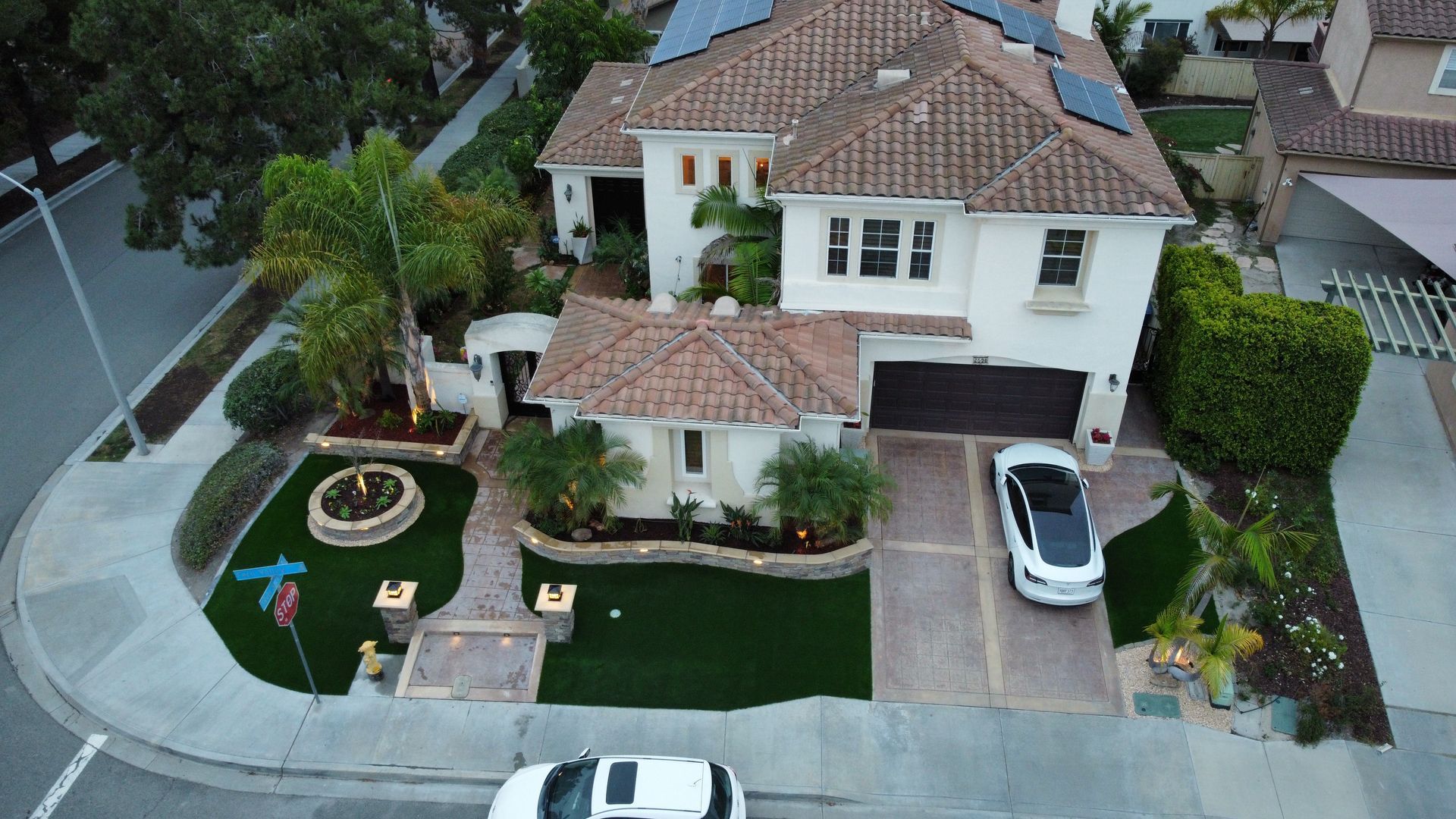 A two-story house with a Tesla parked in the driveway and a small building in front.