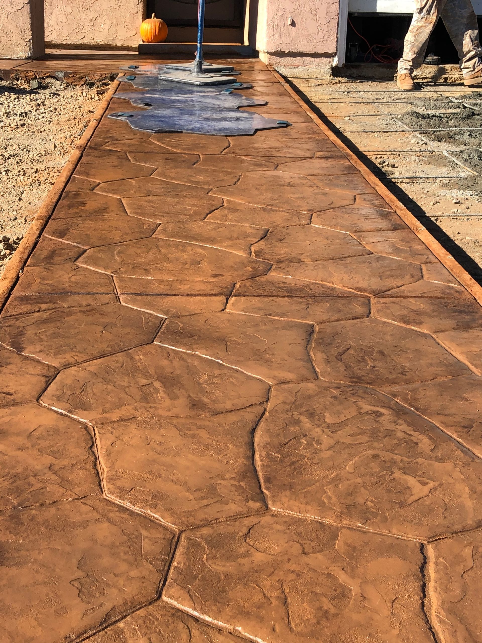 Newly poured, stamped concrete walkway with a stone pattern. Brown color, with worker in the background.
