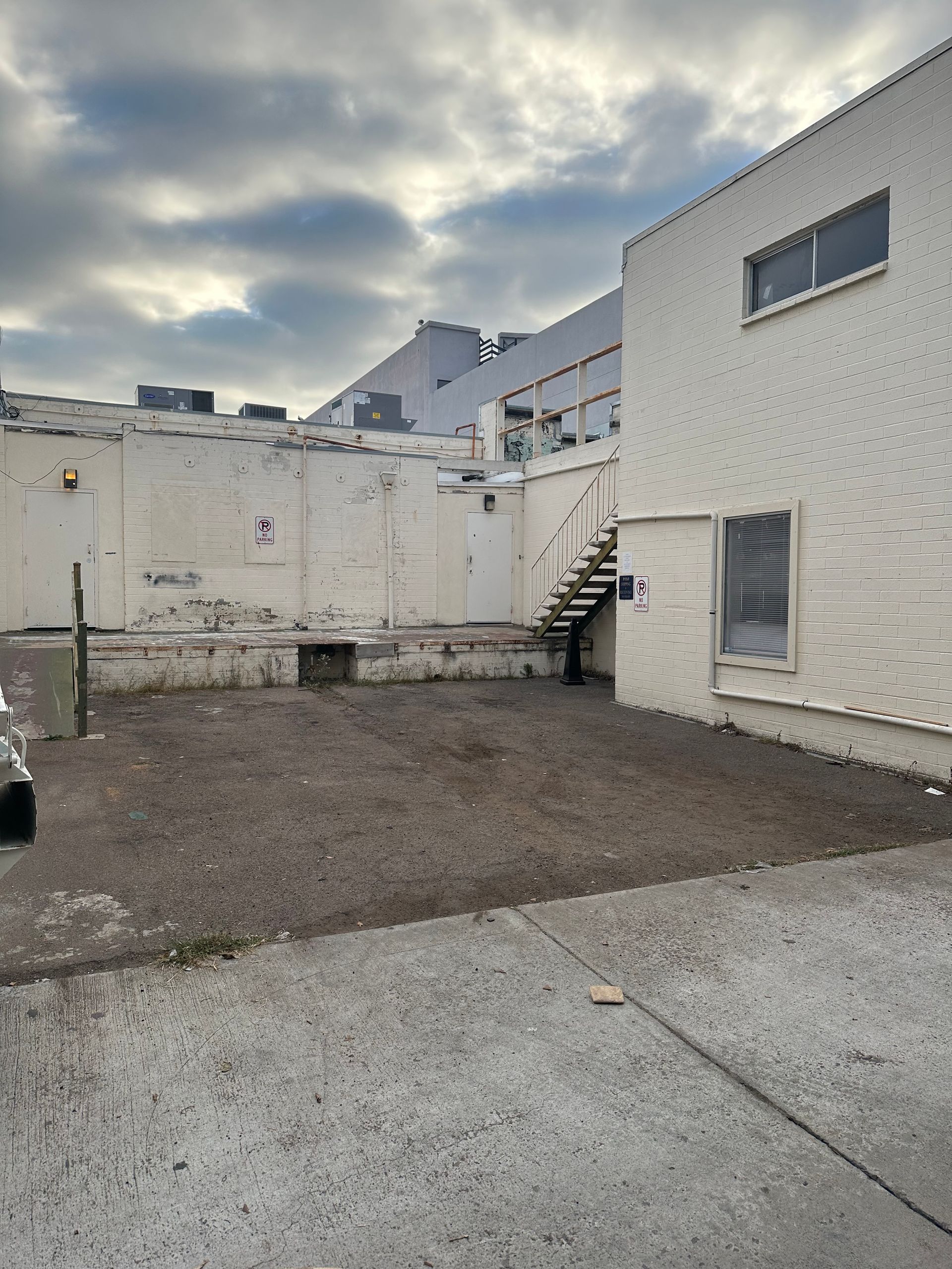 Gravel lot and white buildings. Dark clouds above. Staircase on the right.