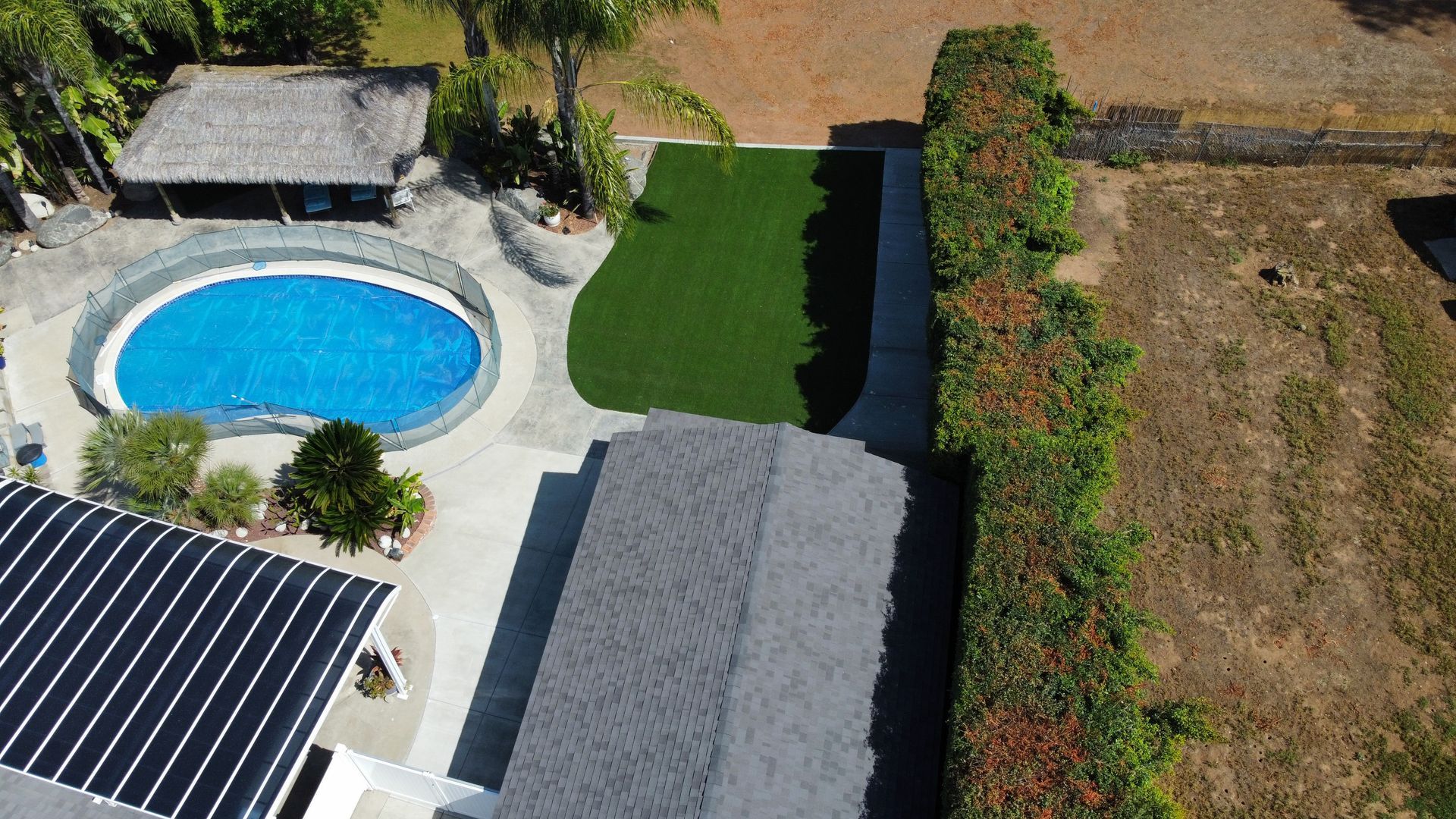 Overhead view of a house with a pool, green lawn, and hedge. A solar panel roof is visible.