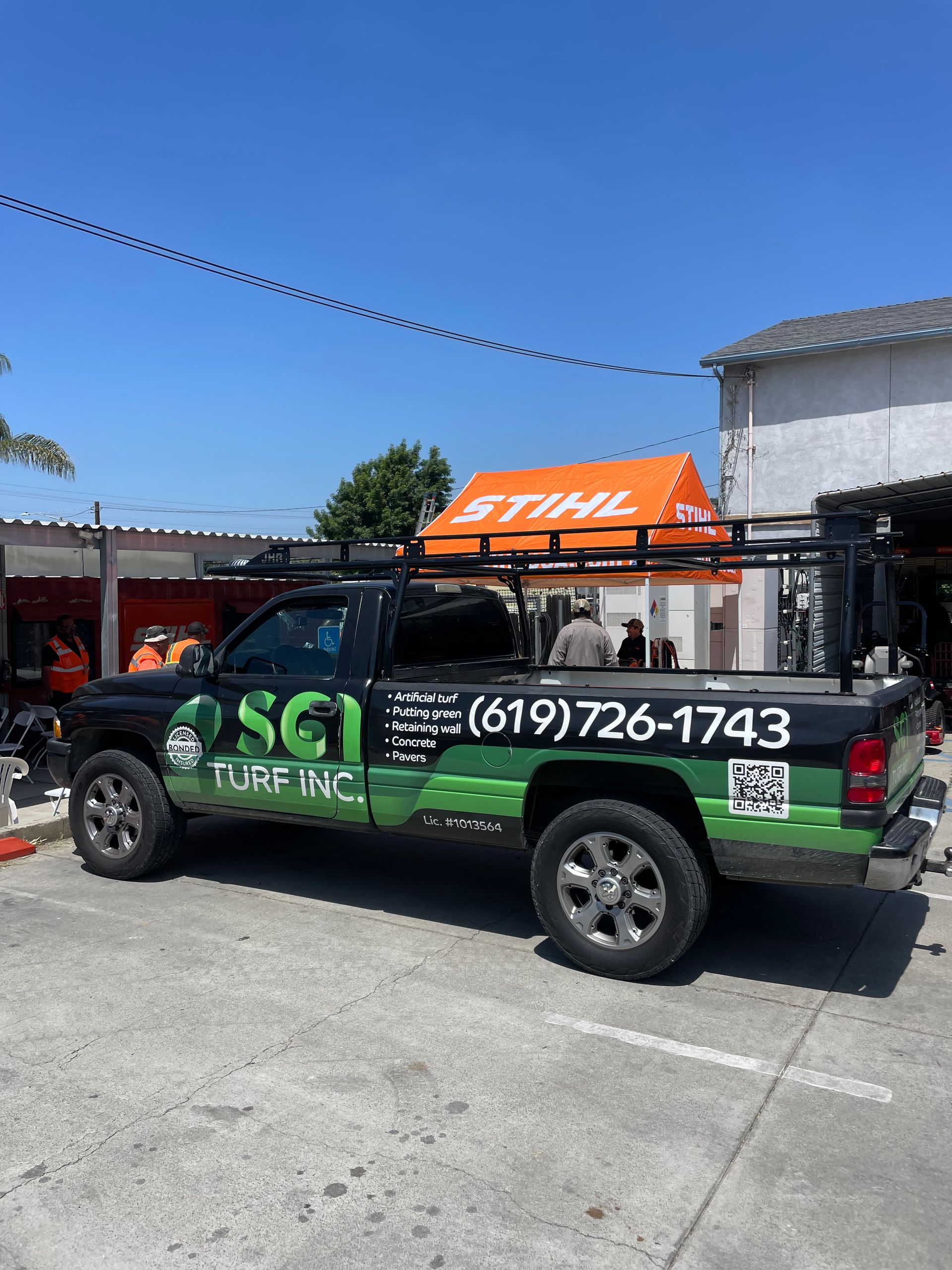 Black truck with green and white logo parked, sky in background.  (619)726-1743 on the side.