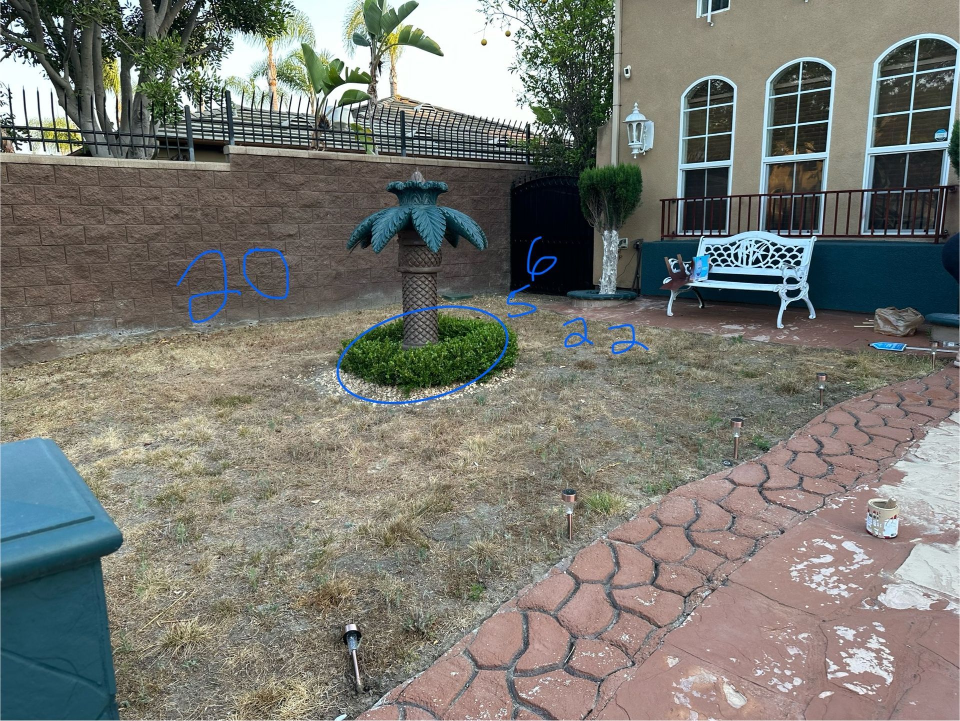 A yard with a palm tree statue, a white bench, and a brown, dry lawn.
