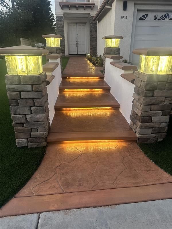 Stone steps and walkway illuminated with warm lighting, leading to a home entrance.